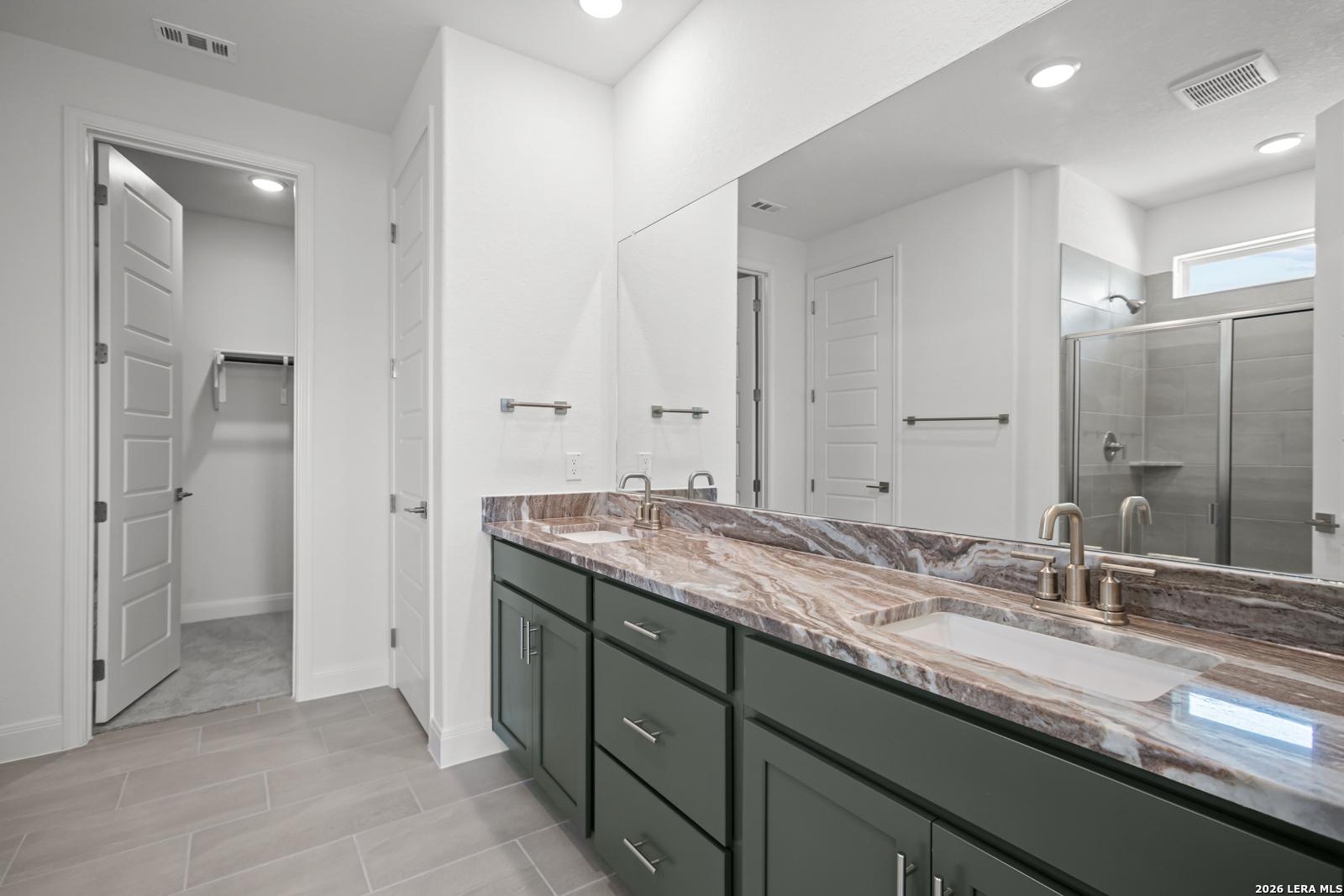 Modern primary bathroom with double vanity, stone countertop, and walk-in closet in The Lanier G home, Castroville, TX.