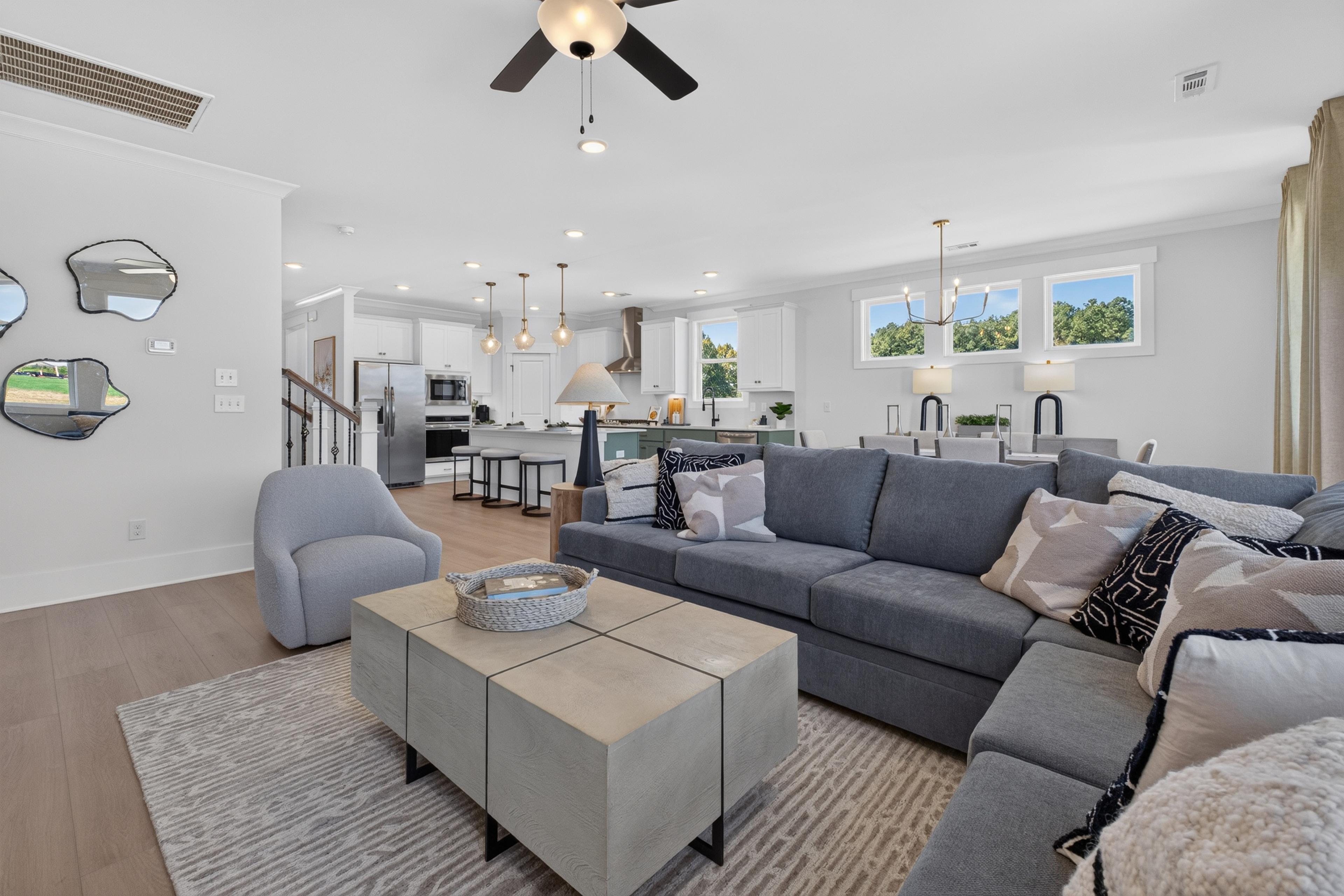 Open-concept great room at Evergreen Mill in Madison, Alabama by Davidson Homes with gray sectional sofa and white kitchen