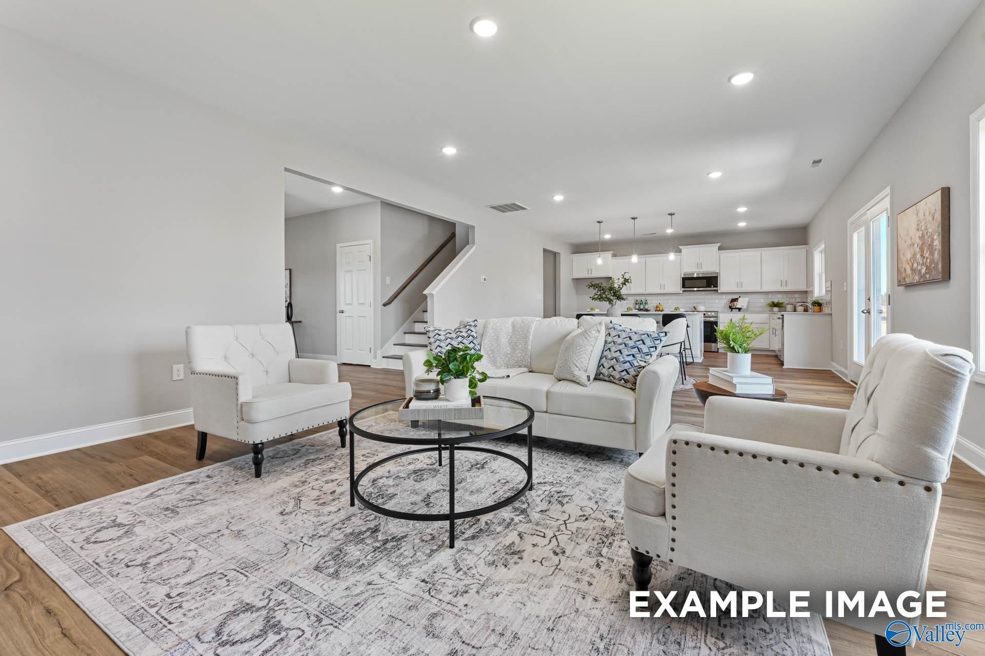 Bright living room with white sectional sofa, glass coffee table, and open kitchen in Davidson Homes The Chelsea B, Toney, Alabama
