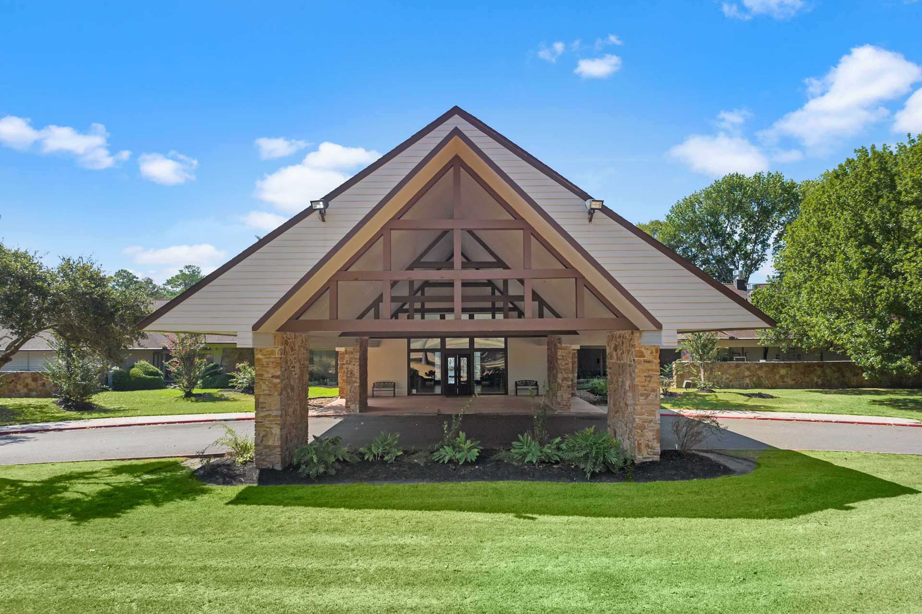 Grand entrance pavilion at Enclave at Newport in Crosby Texas with gabled wooden roof stone pillars and lush landscaping