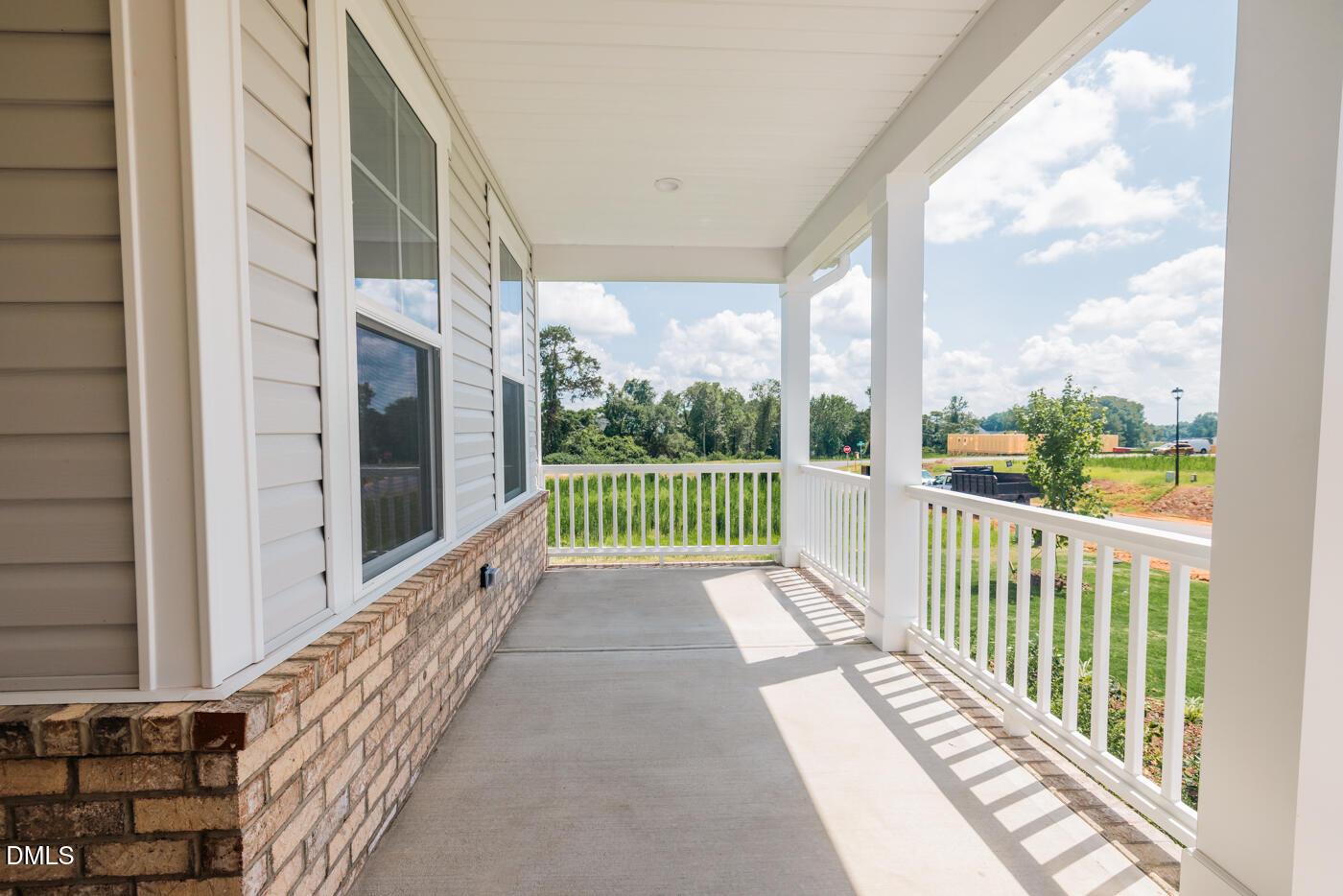 Covered porch with white railing and columns overlooking green yard and fields in The Hickory II C, Woodland Crossing, Zebulon, NC