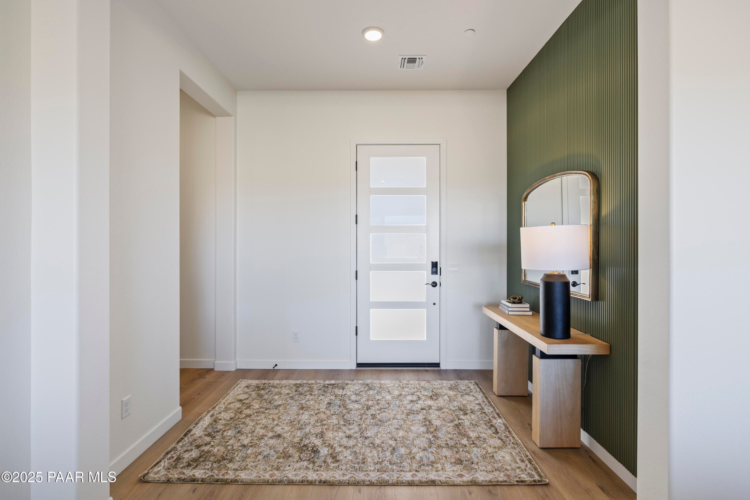 Modern entry foyer with white glass-paneled door, wooden console table, round mirror, lamp on green accent wall in Prescott AZ home