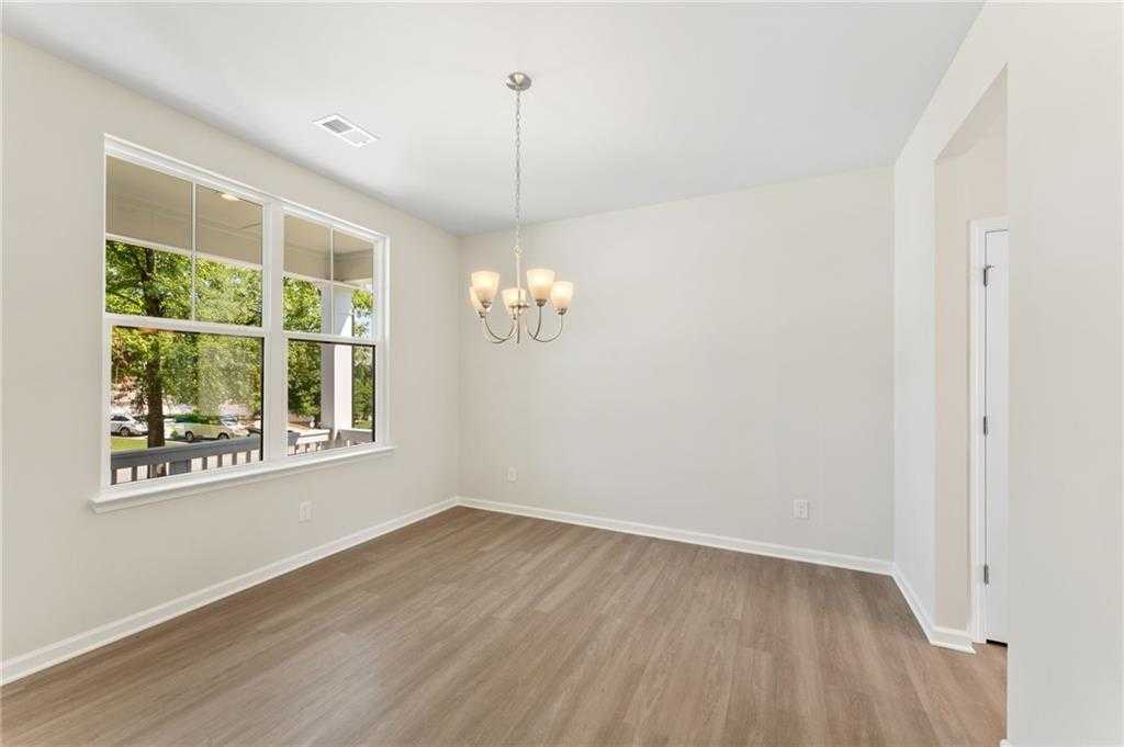 Elegant dining room with large windows overlooking greenery, modern chandelier, hardwood floors in Davidson Homes The Ash B, Riverwood, Dallas, GA