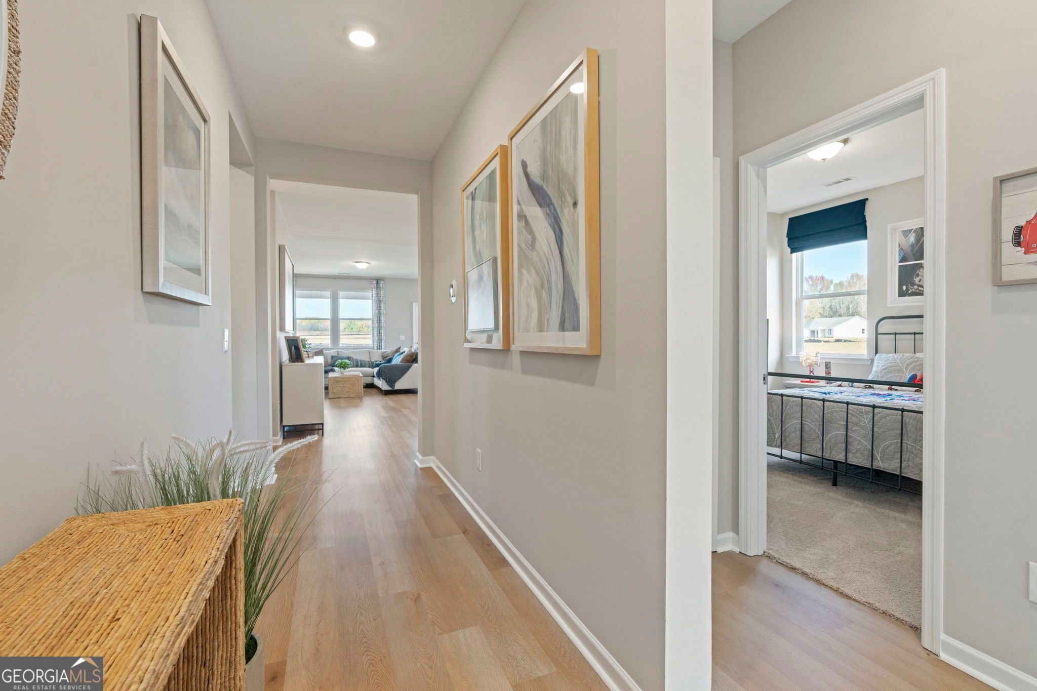 Bright hallway with hardwood floors, modern abstract art, potted plant, leading to living room and bedroom in Evermore Homes The Phoenix, Perry, GA