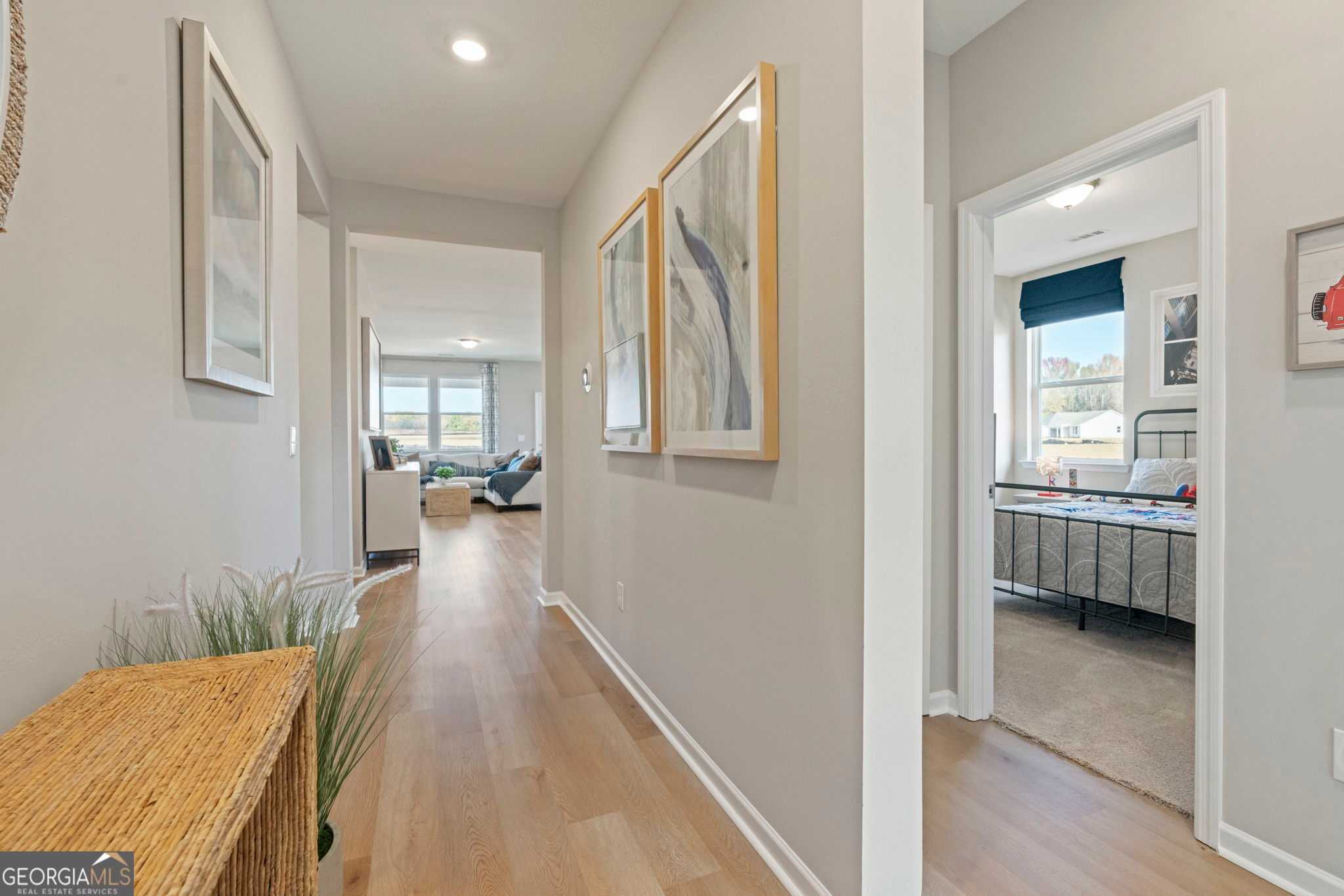 Bright hallway with hardwood floors, modern abstract art, potted plant, leading to living room and bedroom in Evermore Homes The Phoenix, Perry, GA