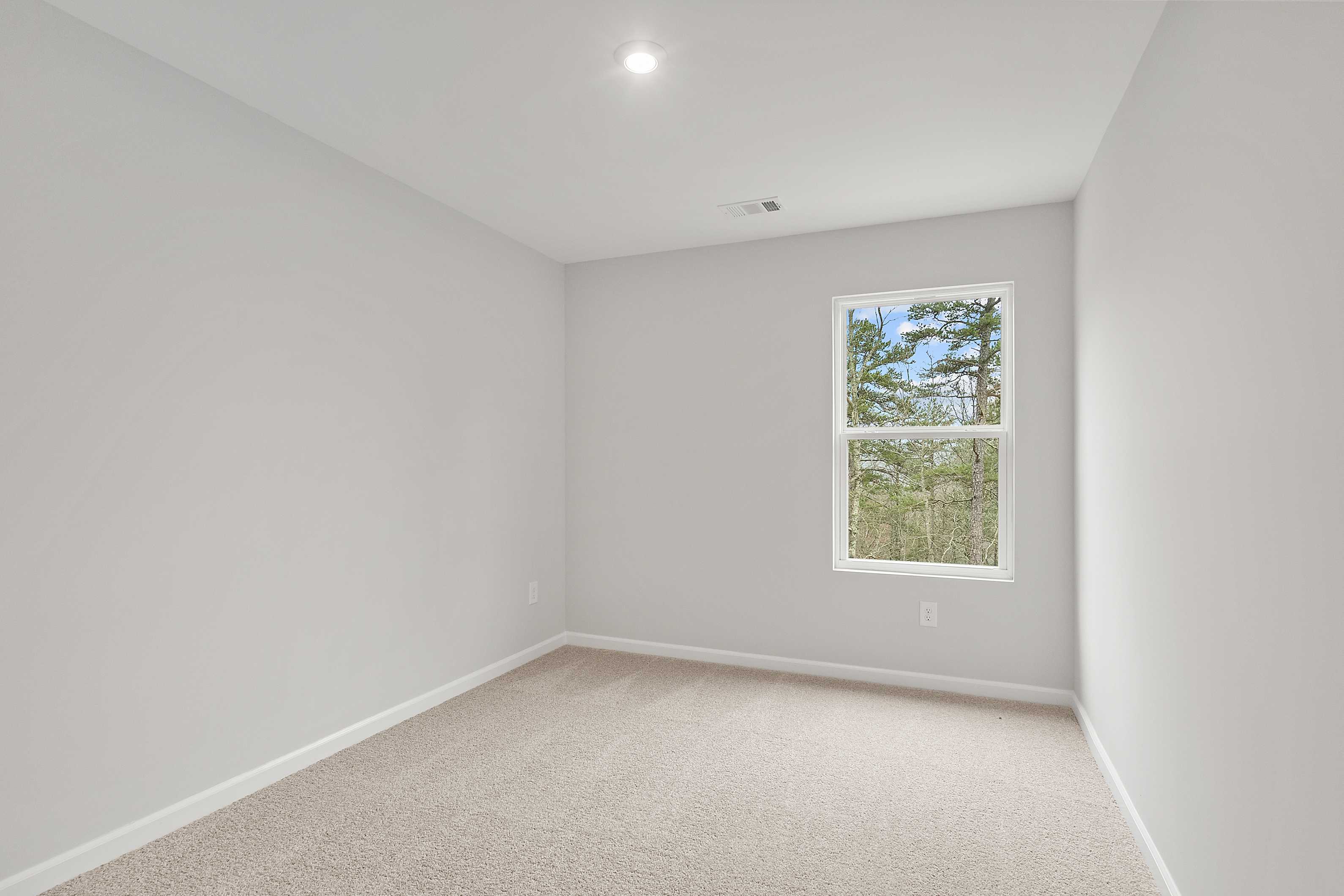 Spacious empty bedroom in The Durant A featuring light gray walls, beige carpet, and large window with pine tree view