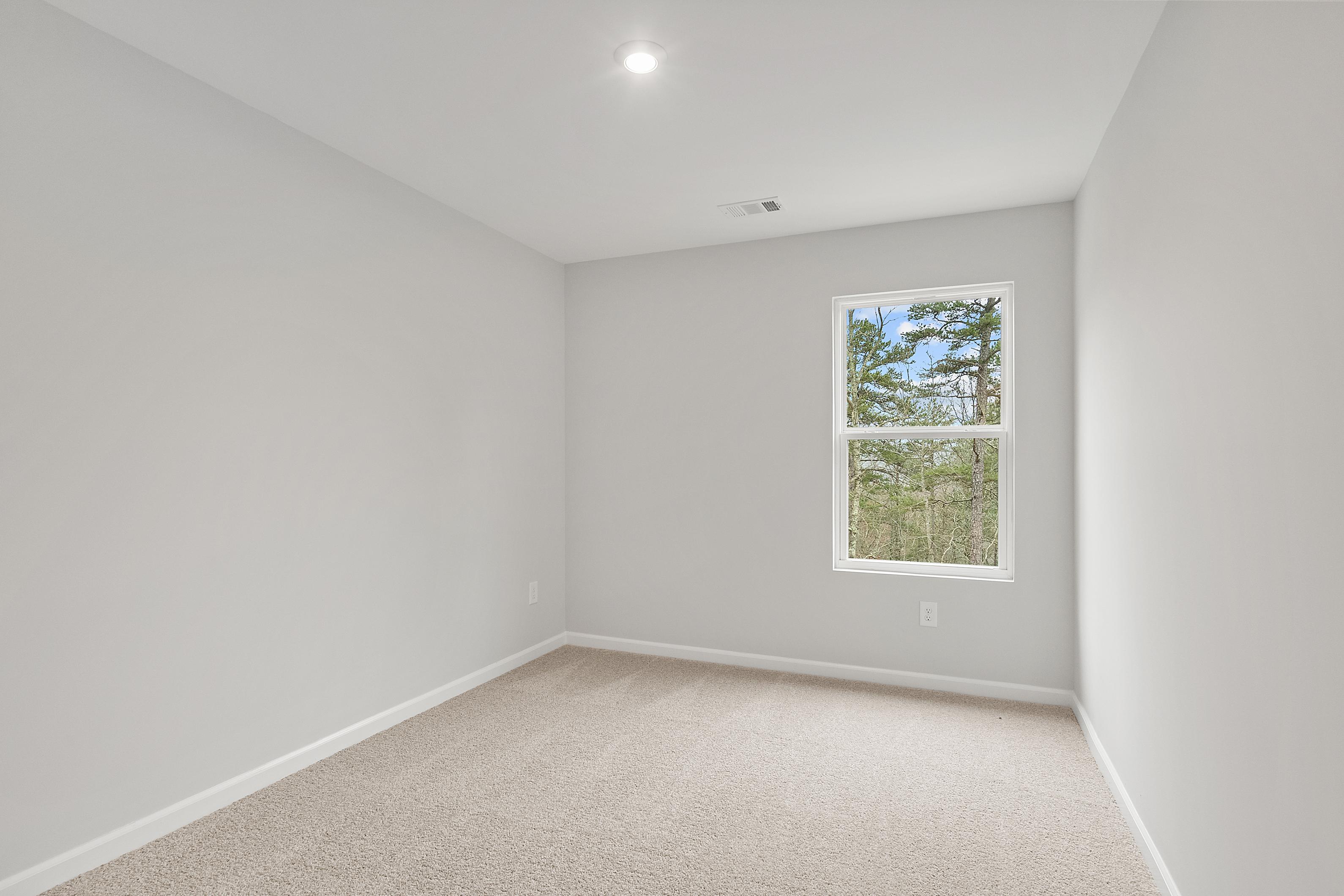 Spacious empty bedroom in The Durant A featuring light gray walls, beige carpet, and large window with pine tree view