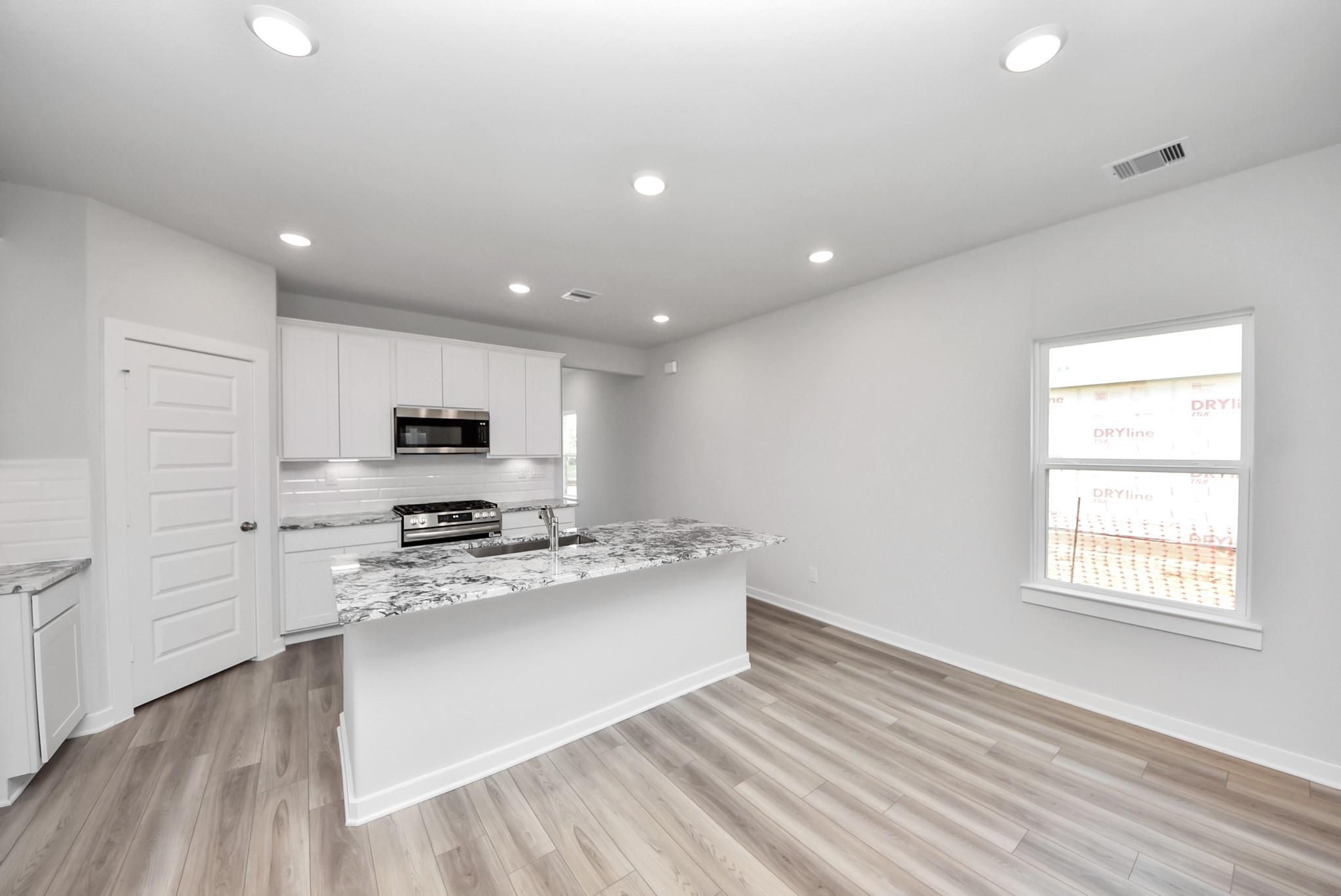 Modern kitchen with granite island and white cabinets in The Sabine E floor plan at Windmill Estates, Magnolia, Texas.