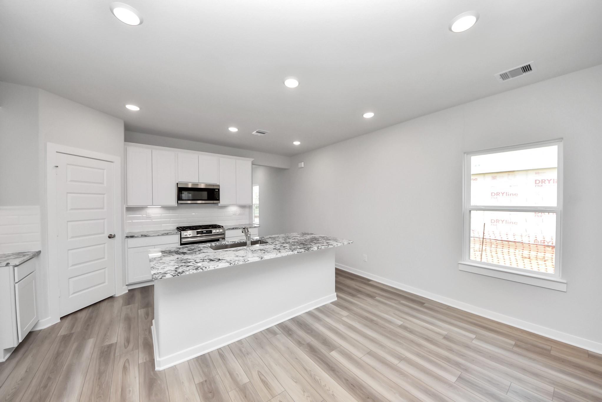 Modern kitchen with granite island and white cabinets in The Sabine E floor plan at Windmill Estates, Magnolia, Texas.