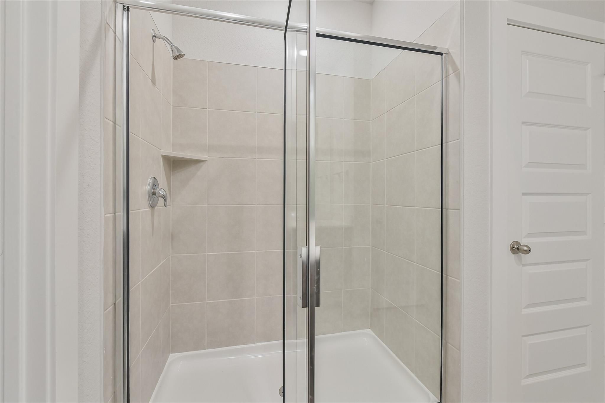 Modern glass shower enclosure with white subway tile walls and built-in shelves in The Brazos E master bath, Davidson Homes, Cleveland, TX