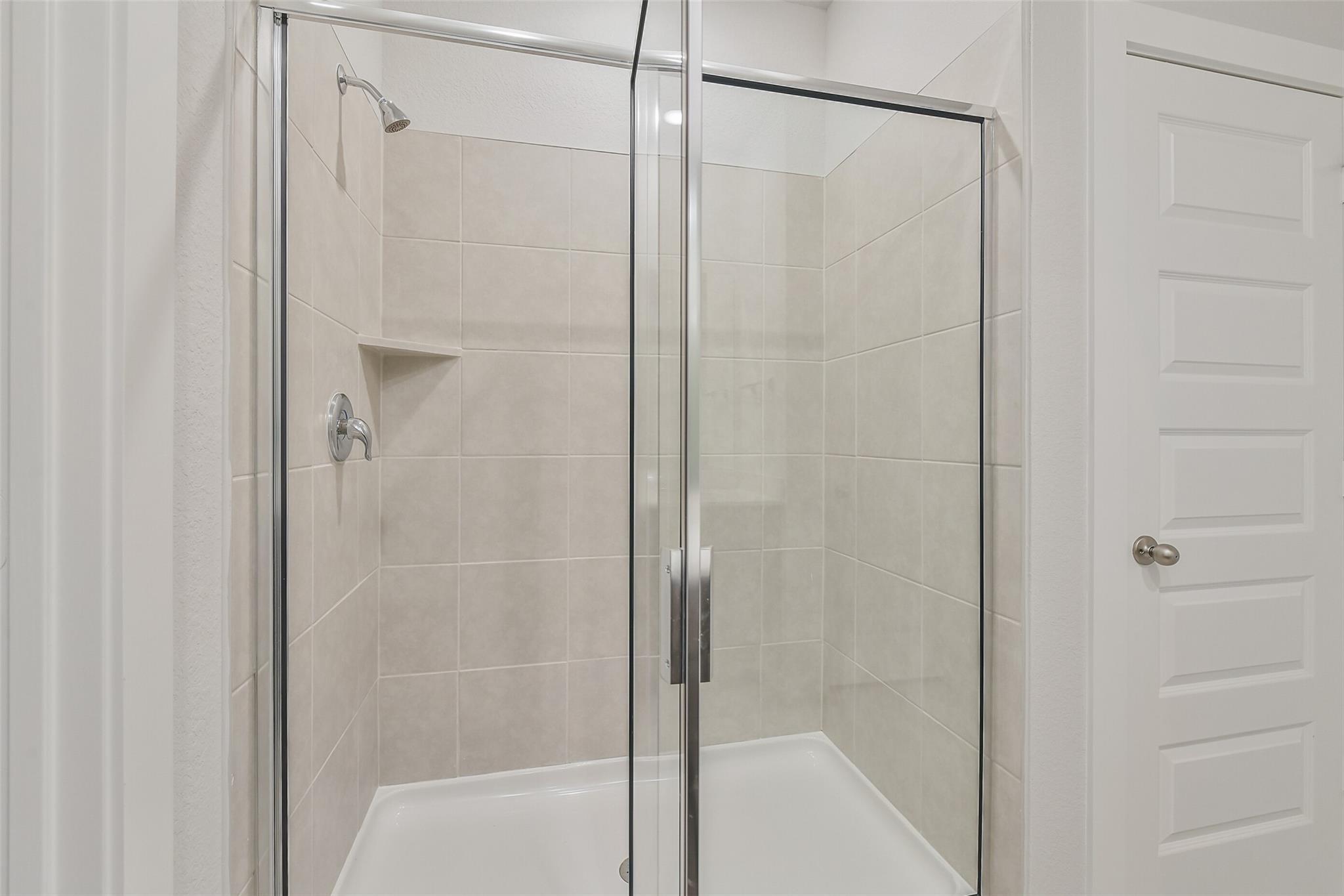 Modern glass shower enclosure with white subway tile walls and built-in shelves in The Brazos E master bath, Davidson Homes, Cleveland, TX