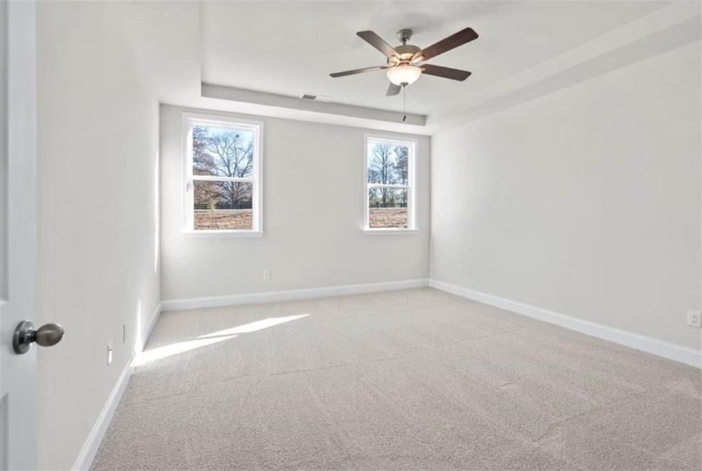 Spacious bedroom with tray ceiling and ceiling fan in The Ash C floor plan at Wehunt Meadows, Hoschton, Georgia.