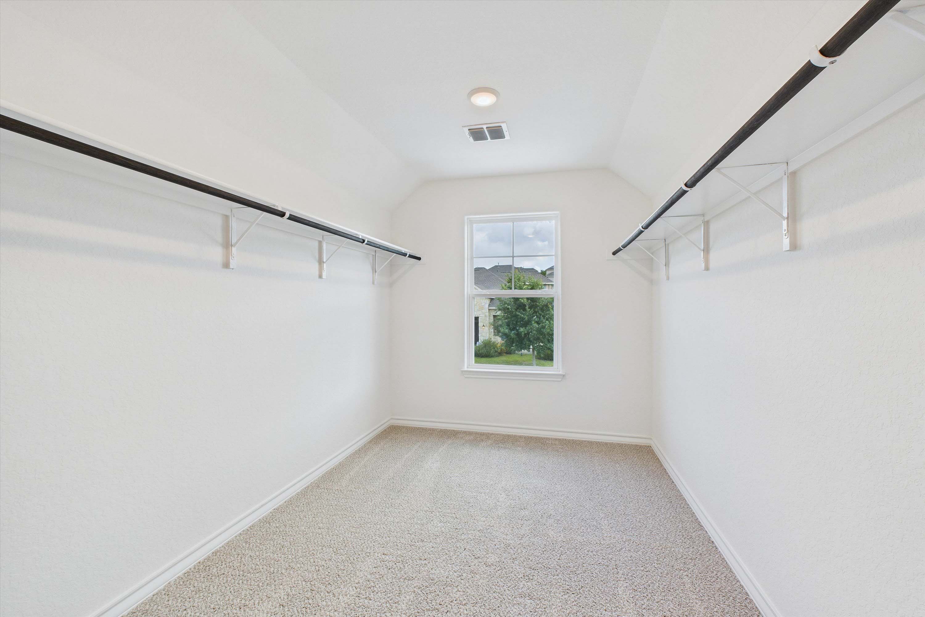 Spacious walk-in closet in The Danbury master suite featuring white walls, carpeted flooring, and dual hanging rods.