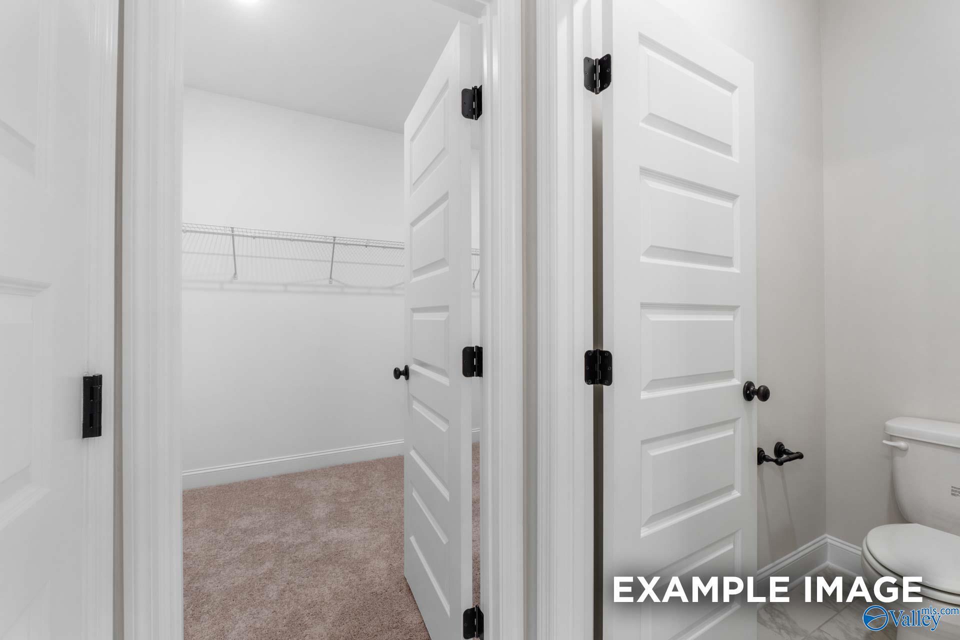 Spacious walk-in closet with hanging rods and shelves adjacent to master bathroom toilet in Davidson Homes The Finleigh, Meridianville, AL