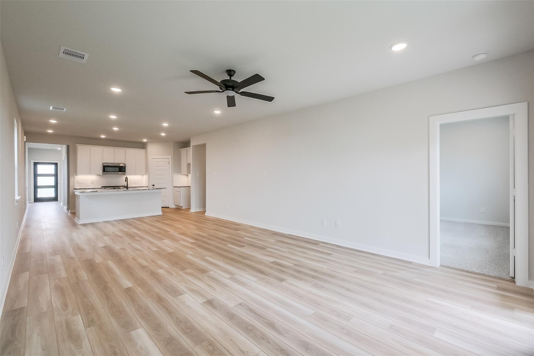 Open-concept kitchen and living area with white cabinets, island, hardwood floors, and ceiling fan in Davidson Homes San Marcos E, Beasley Texas