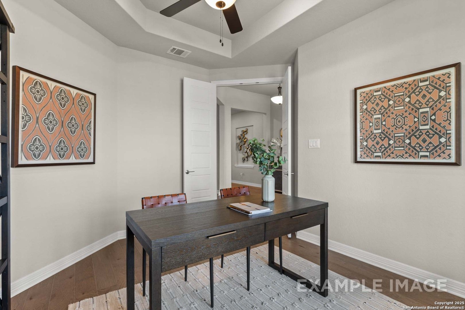 Elegant home office with dark wood desk, leather chairs, abstract wall art, and tray ceiling in The Summerlin B, Castroville, Texas