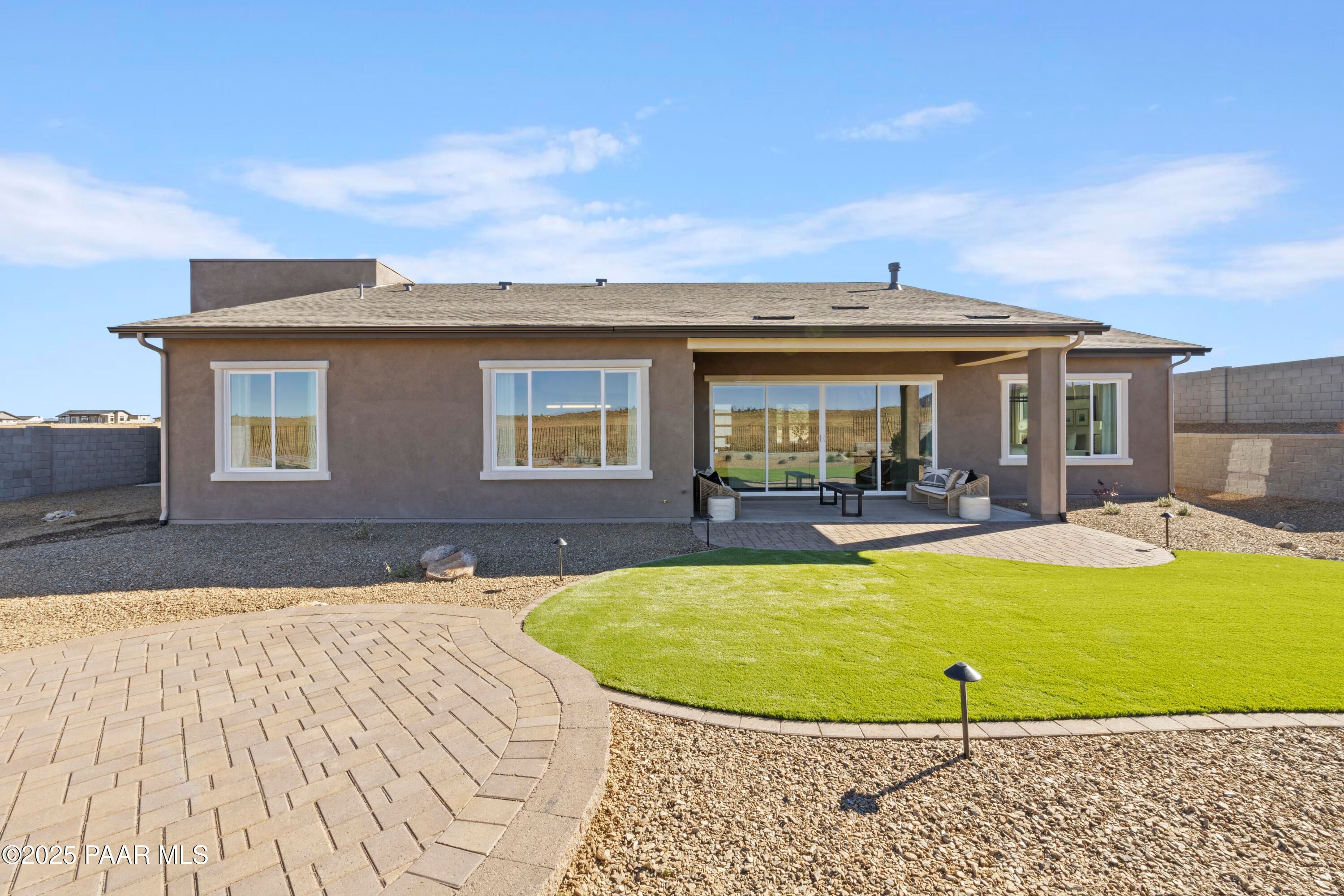 Covered back patio with large windows overlooking gravel yard, green turf, and paver path in Davidson Homes The Blaze D, Prescott AZ