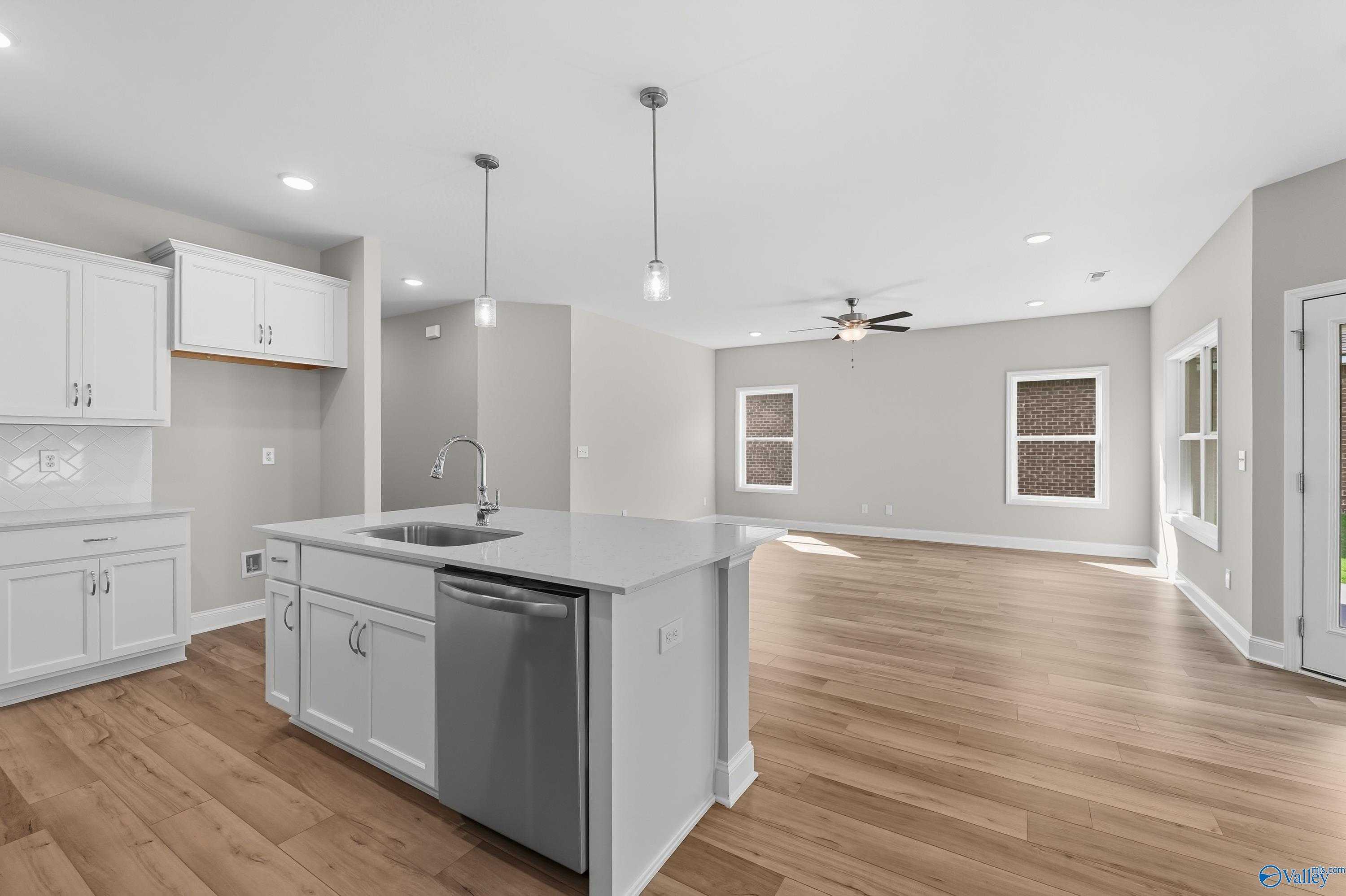Modern open-concept kitchen with white shaker cabinets, quartz island sink, stainless dishwasher, and ceiling fan in Davidson Homes Franklin C, Meridianville AL