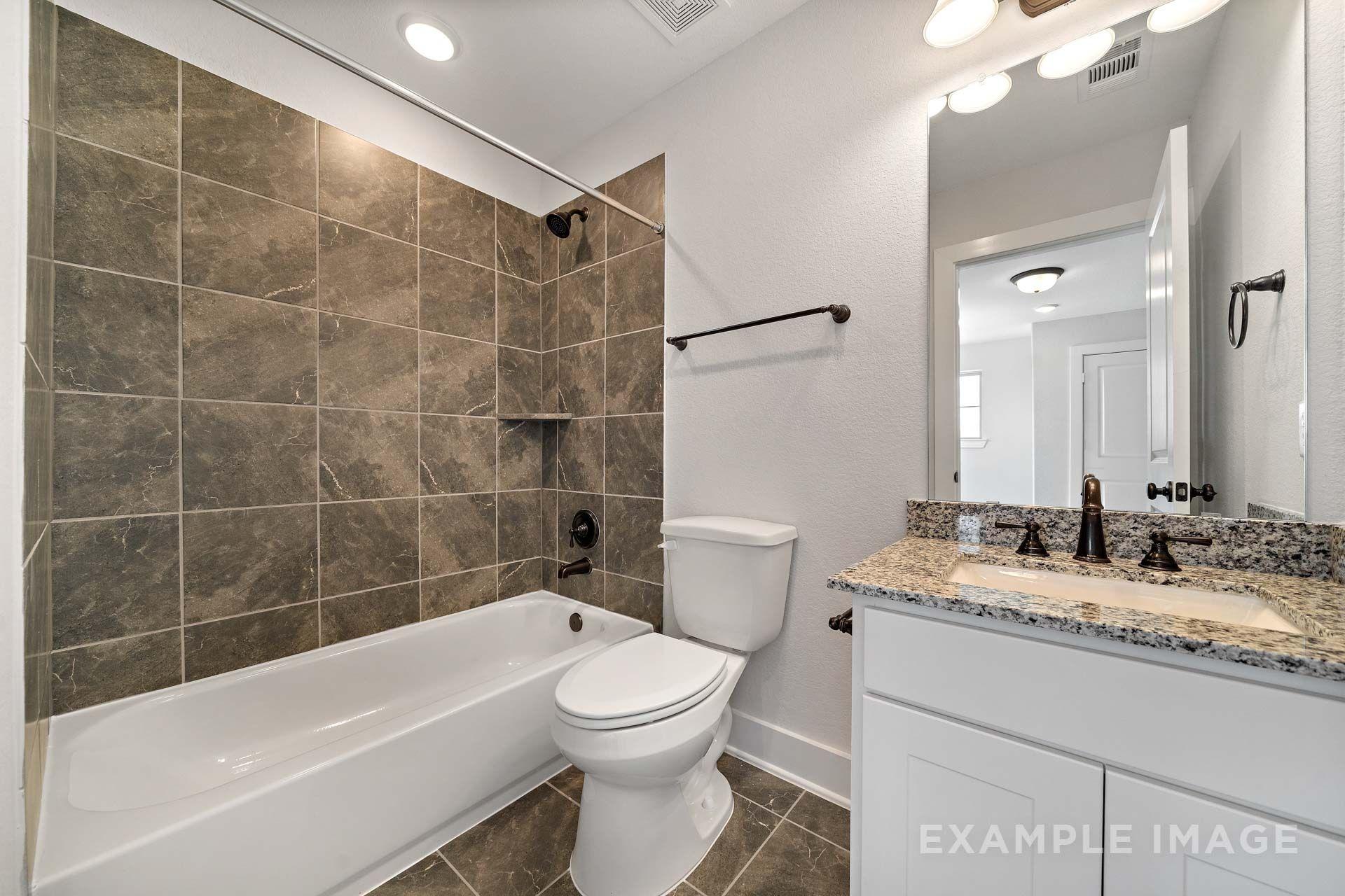 Bathroom in The Victoria by Davidson Homes featuring tiled tub shower, granite vanity, and white cabinetry in Texas City, TX