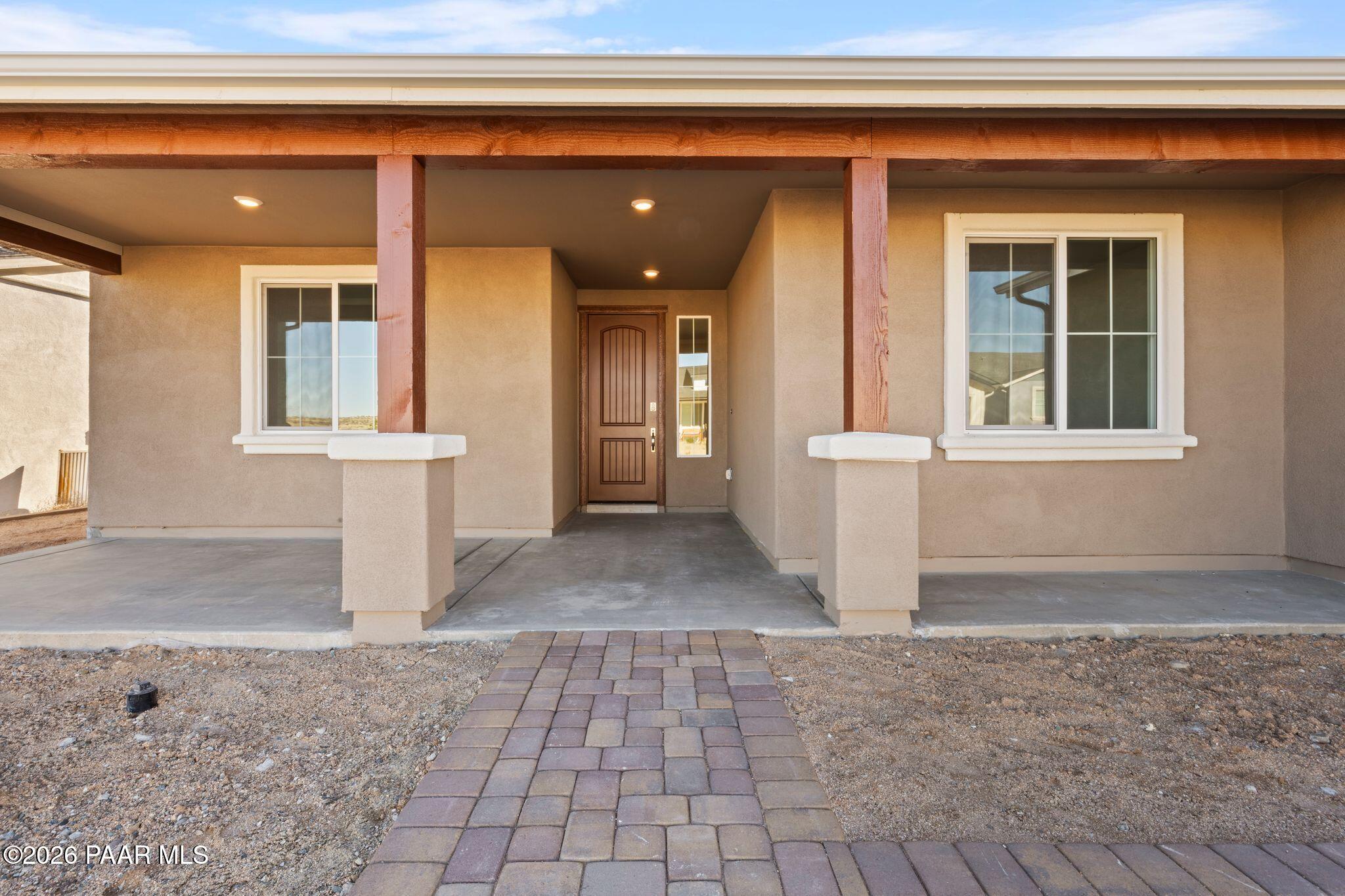 Tan stucco single-story home exterior with covered porch, wooden beams, double doors, and brick walkway in Westwood, Prescott, AZ