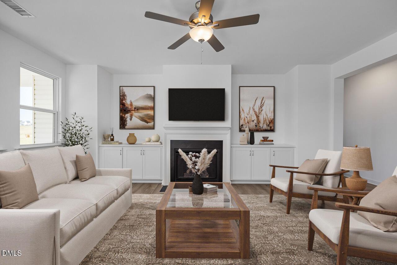 Cozy living room with beige sofa, wooden coffee table, wall-mounted TV, ceiling fan in Davidson Homes The Cypress B II, Angier, NC