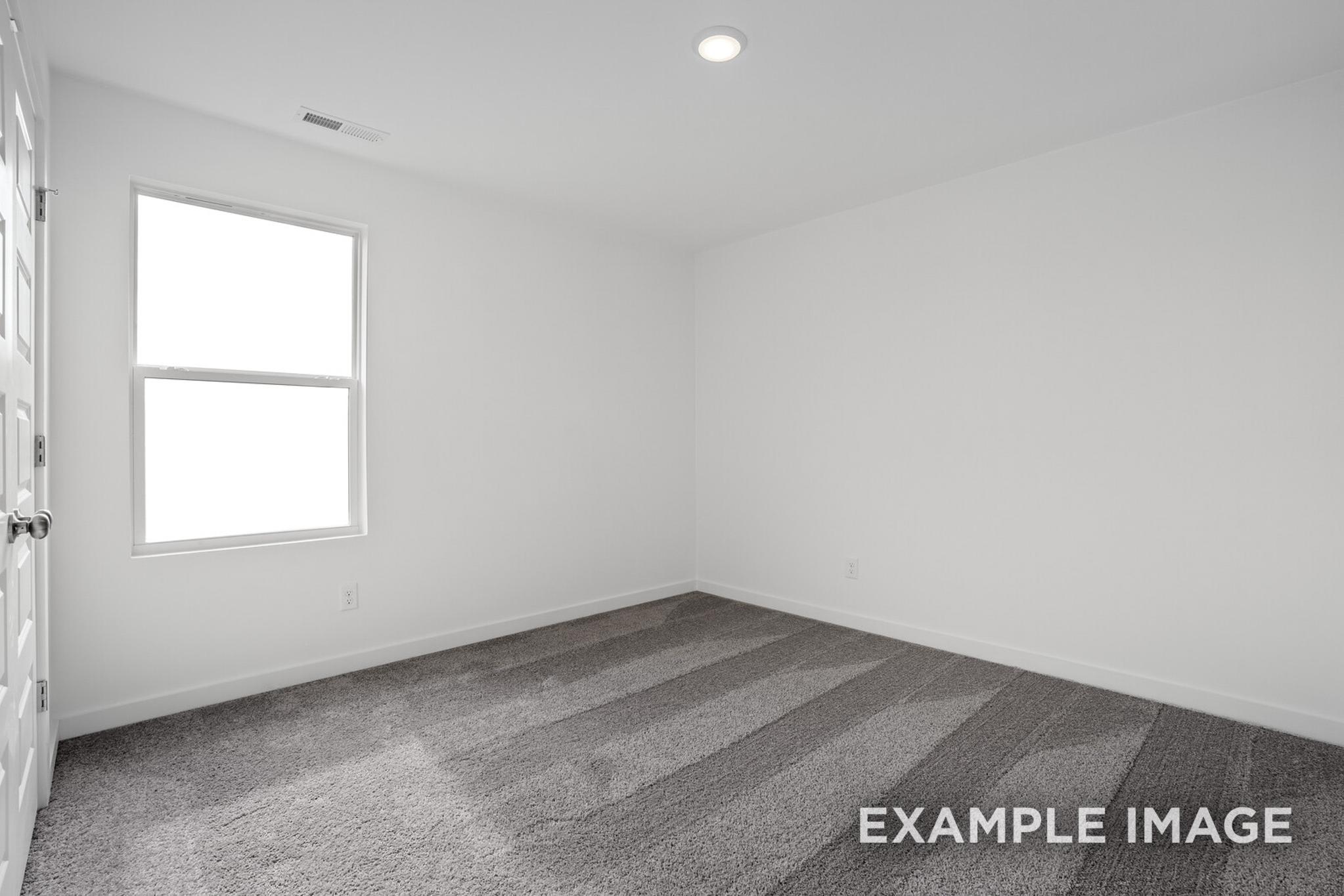 Spacious empty bedroom in The Logan C with white walls, large double window, gray carpet flooring, and open closet door