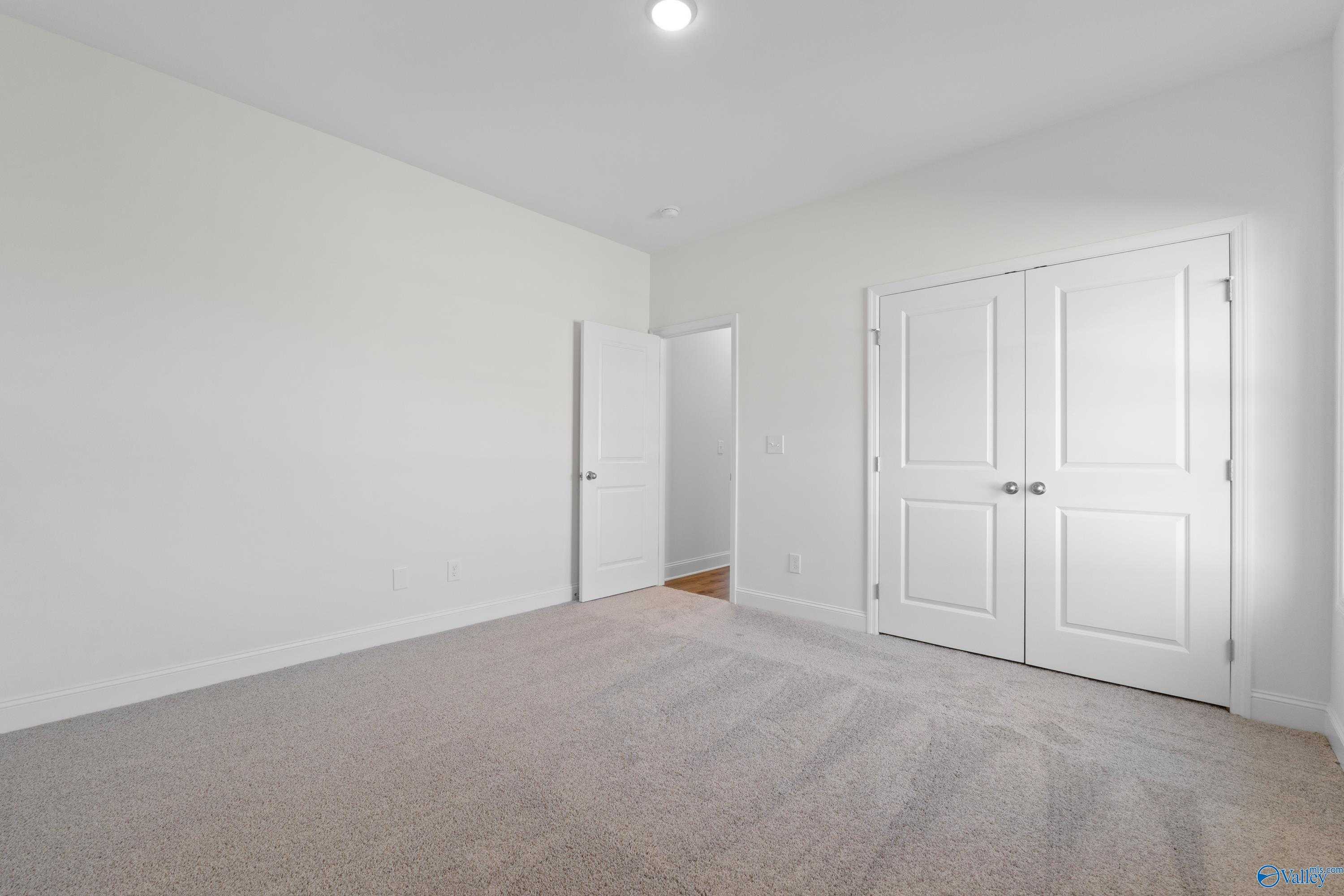 Spacious bedroom featuring white walls, beige carpet, double closet doors, and adjacent bath entry in Davidson Homes The Oxford, Harvest AL