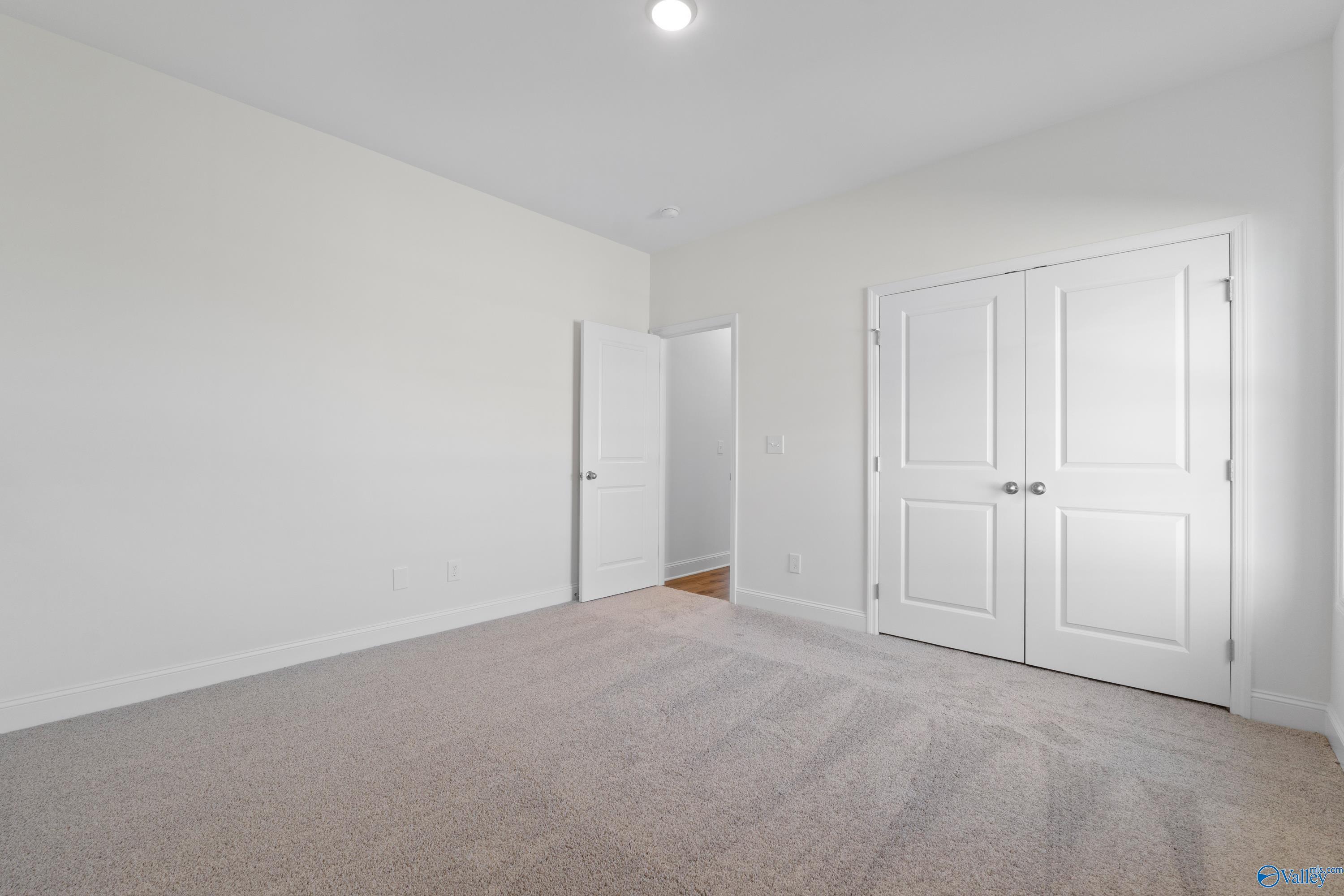 Spacious bedroom featuring white walls, beige carpet, double closet doors, and adjacent bath entry in Davidson Homes The Oxford, Harvest AL