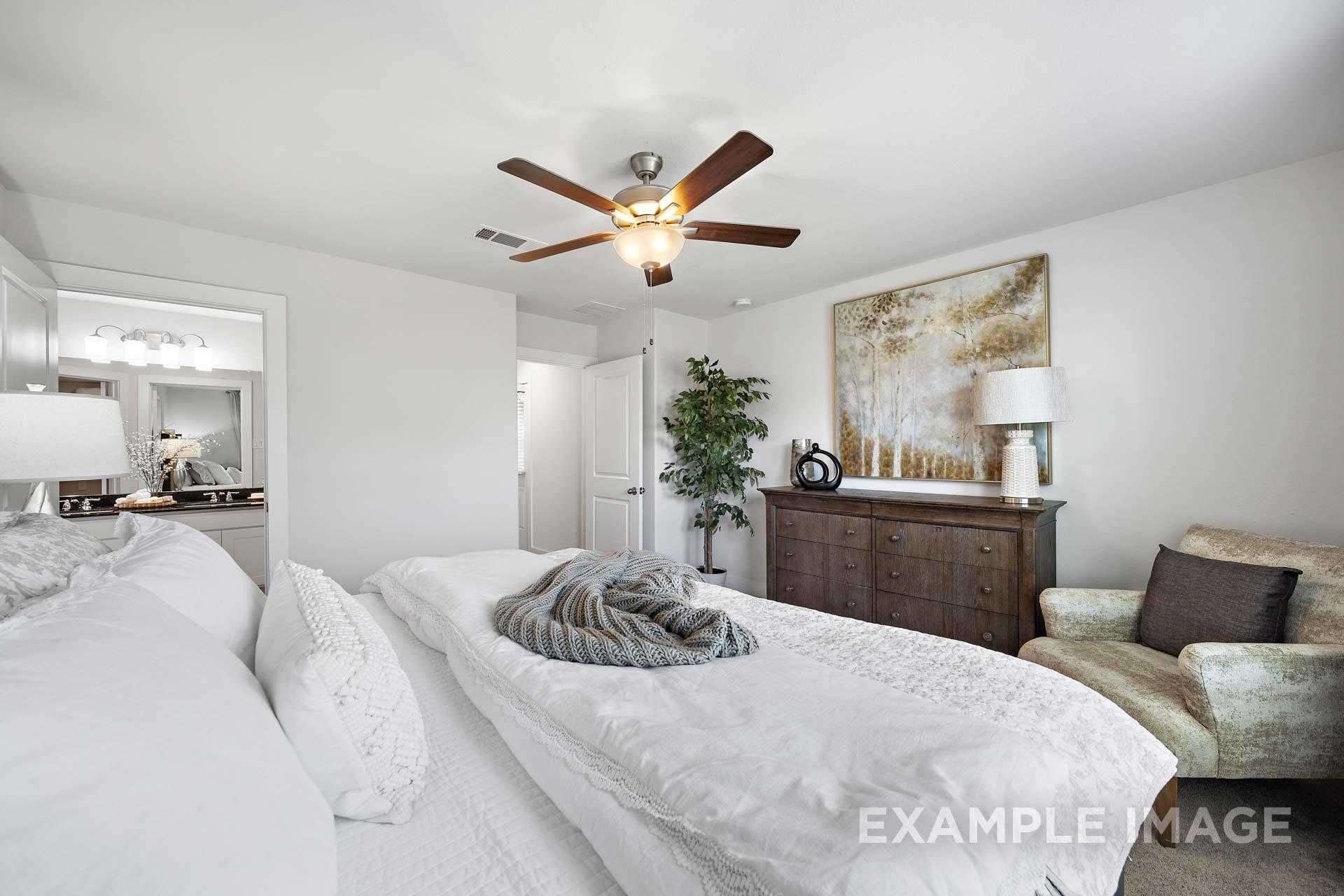 Spacious master bedroom in The Rose B with king bed, white duvet, wooden dresser, armchair, and en-suite bath