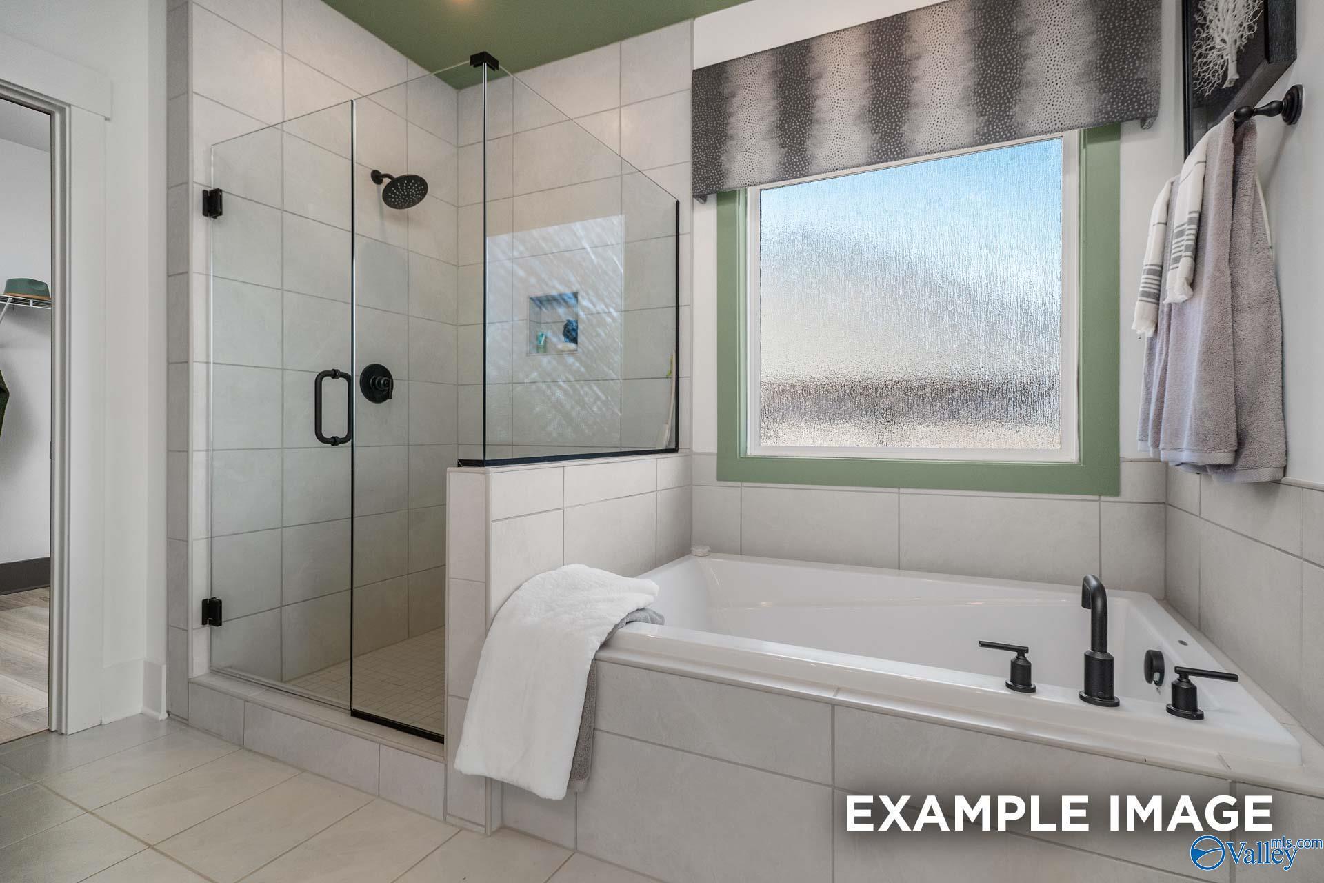 Luxurious master bathroom featuring frameless glass shower, freestanding tub, and green accents in Davidson Homes The Rockford B, Madison, Alabama