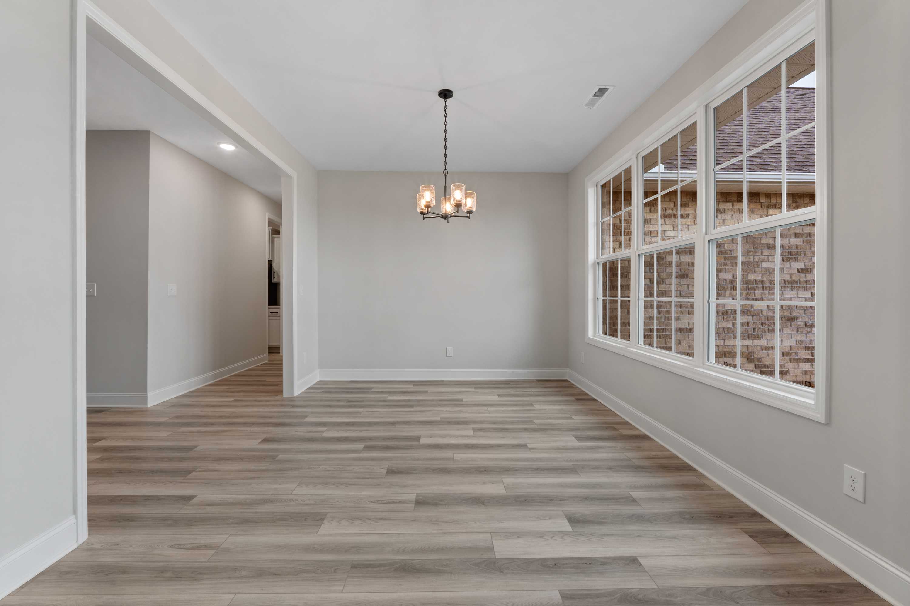 Spacious dining room in The Oxford home design with chandelier, gray walls, large windows, and hardwood floors