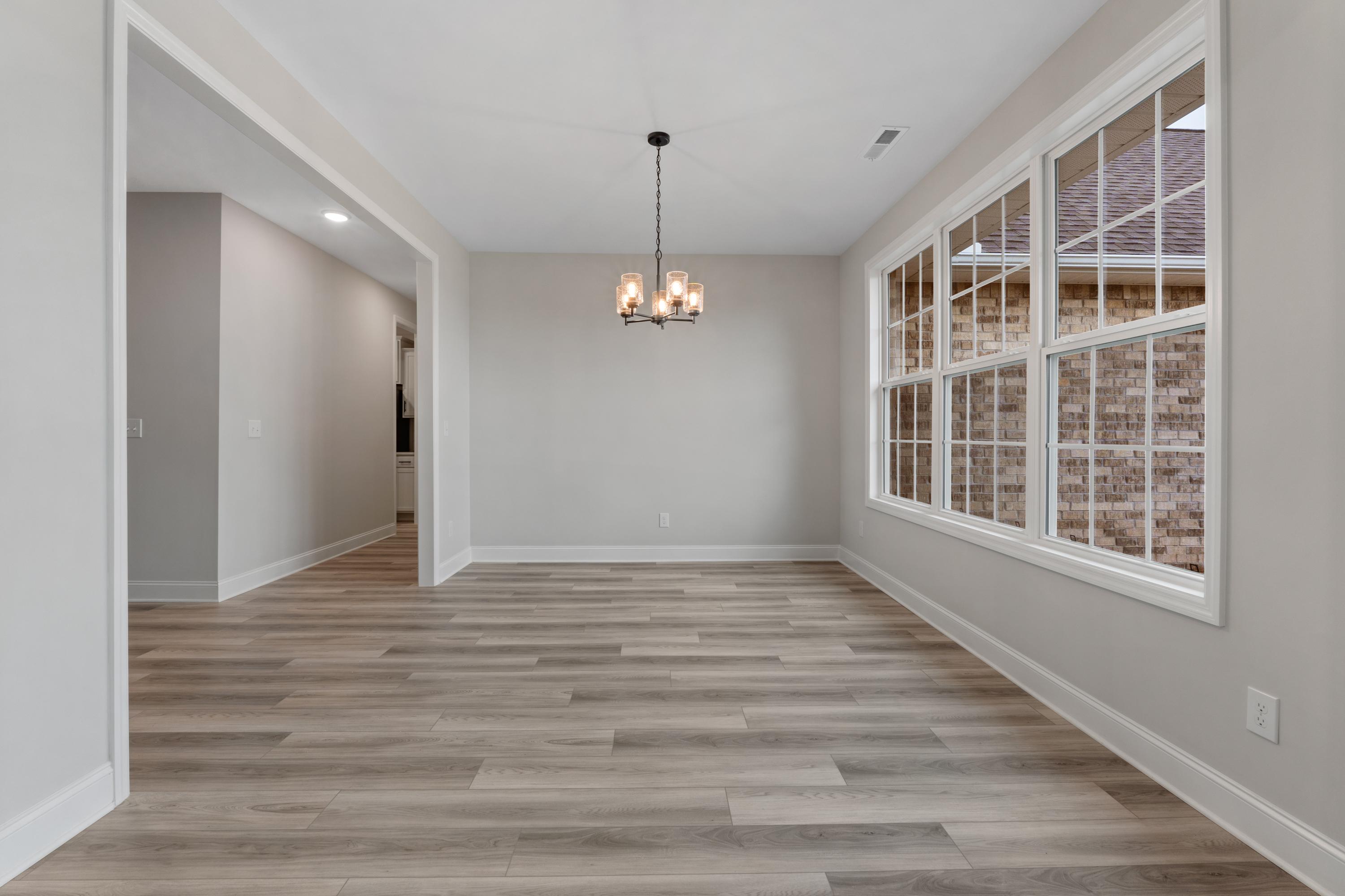 Spacious dining room in The Oxford home design with chandelier, gray walls, large windows, and hardwood floors