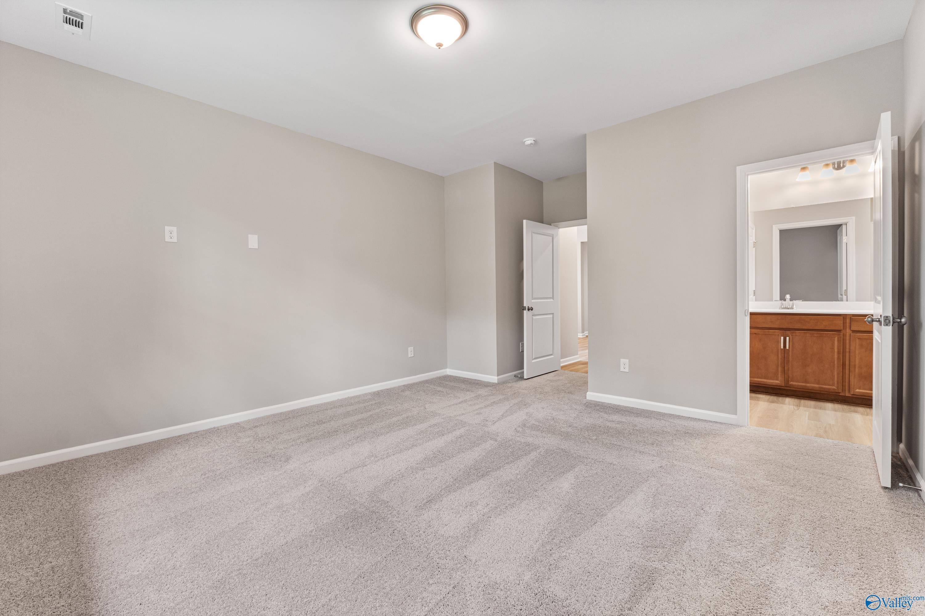 Spacious secondary bedroom with neutral gray walls, plush carpet, and adjacent bathroom in Davidson Homes The Aurora, Fayetteville, TN