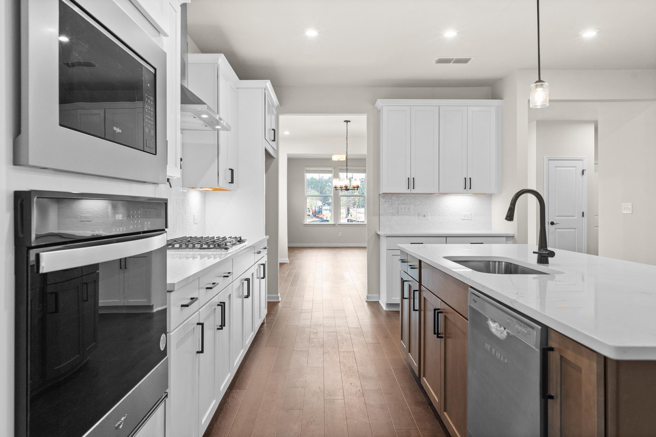 Spacious modern kitchen in The Glenwood home with white shaker cabinets, black appliances, quartz island, and hardwood floors
