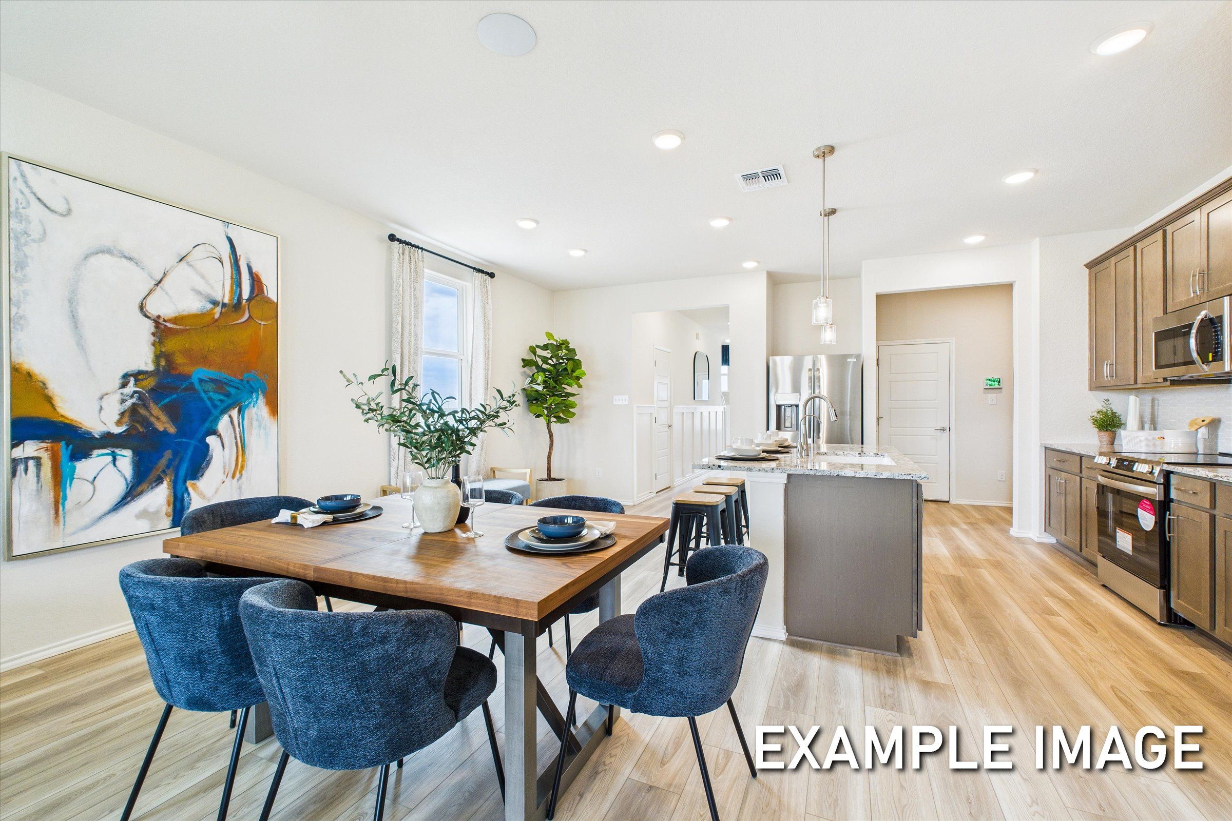 Spacious open-concept dining area in The Brazos A with wooden table, blue chairs, abstract wall art, and modern kitchen island