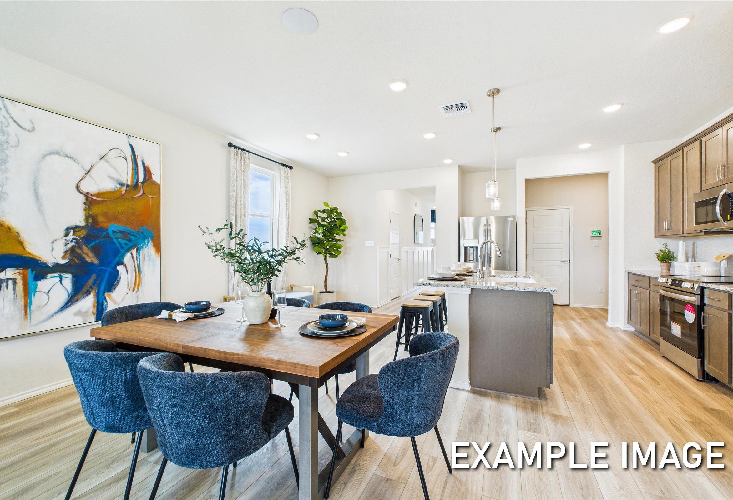 Spacious open-concept dining area in The Brazos A with wooden table, blue chairs, abstract wall art, and modern kitchen island