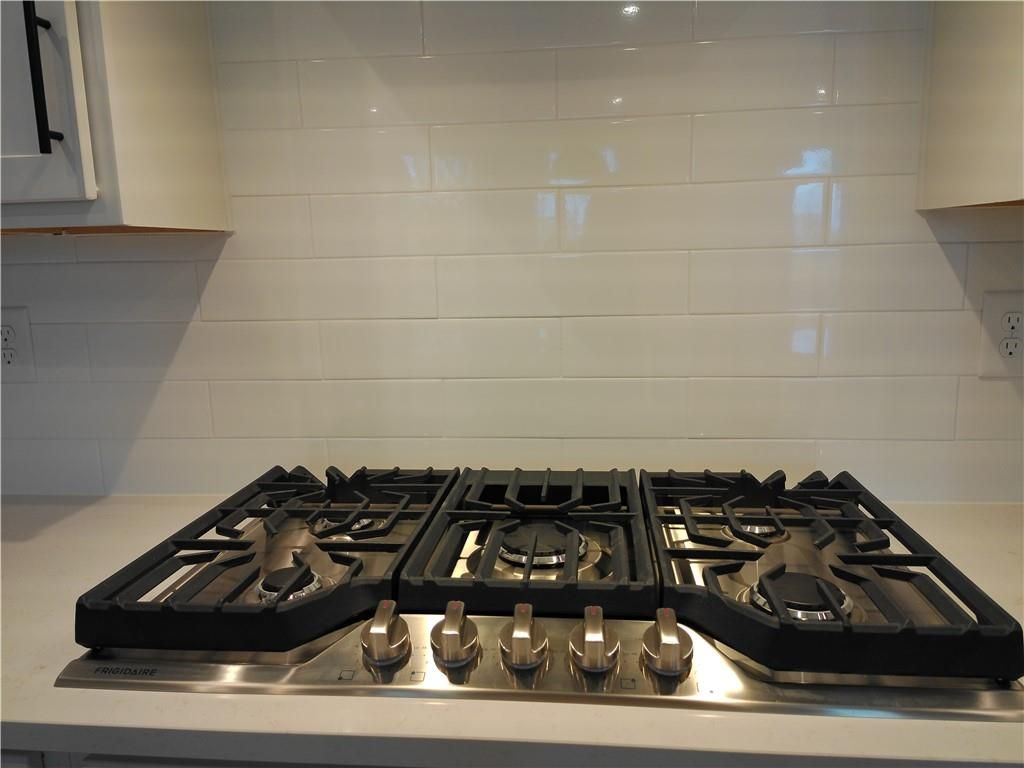 Stainless steel gas cooktop on white quartz countertop with subway tile backsplash in Davidson Homes The Cary A kitchen, Winder, Georgia