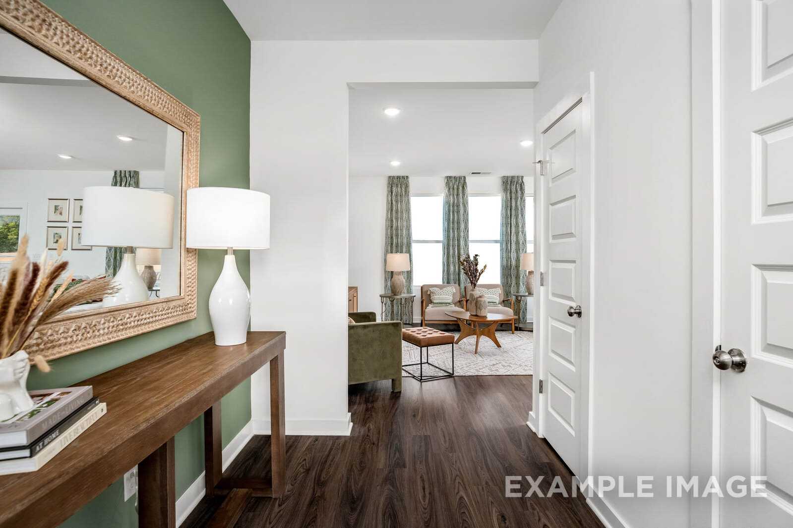 Elegant foyer in The Gordon B showcasing green accent wall, ornate mirror, console table, and open living room view