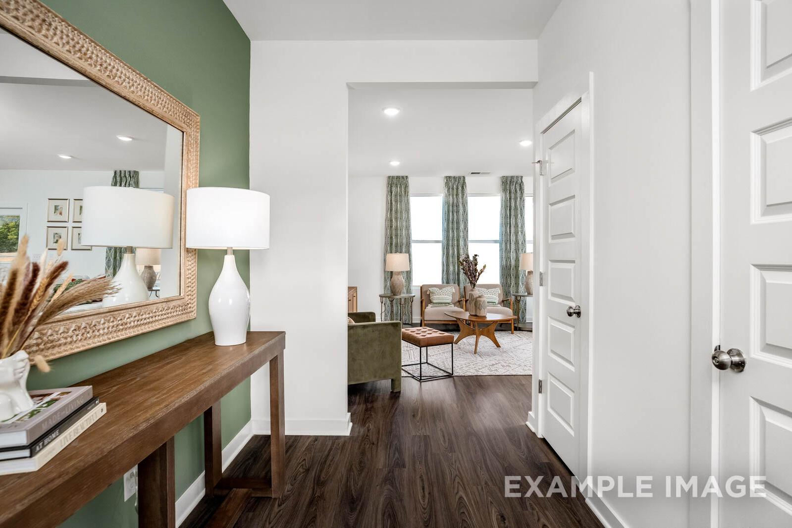 Spacious foyer in The Gordon C home with green accent wall, ornate mirror, console table, lamp, and open living room view with large curtained windows