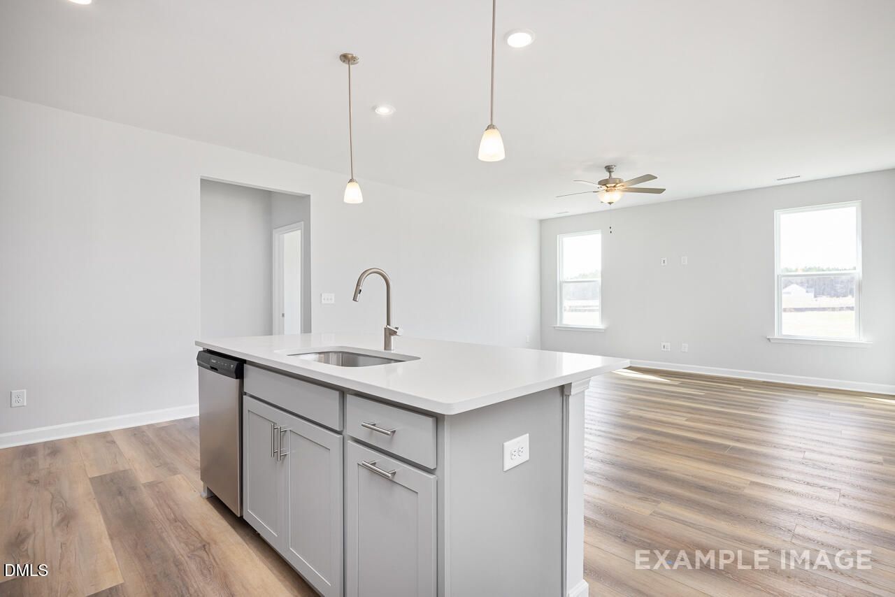 Open-concept kitchen with white quartz island, stainless sink, gray cabinets, hardwood floors in The Daphne C, Zebulon, NC