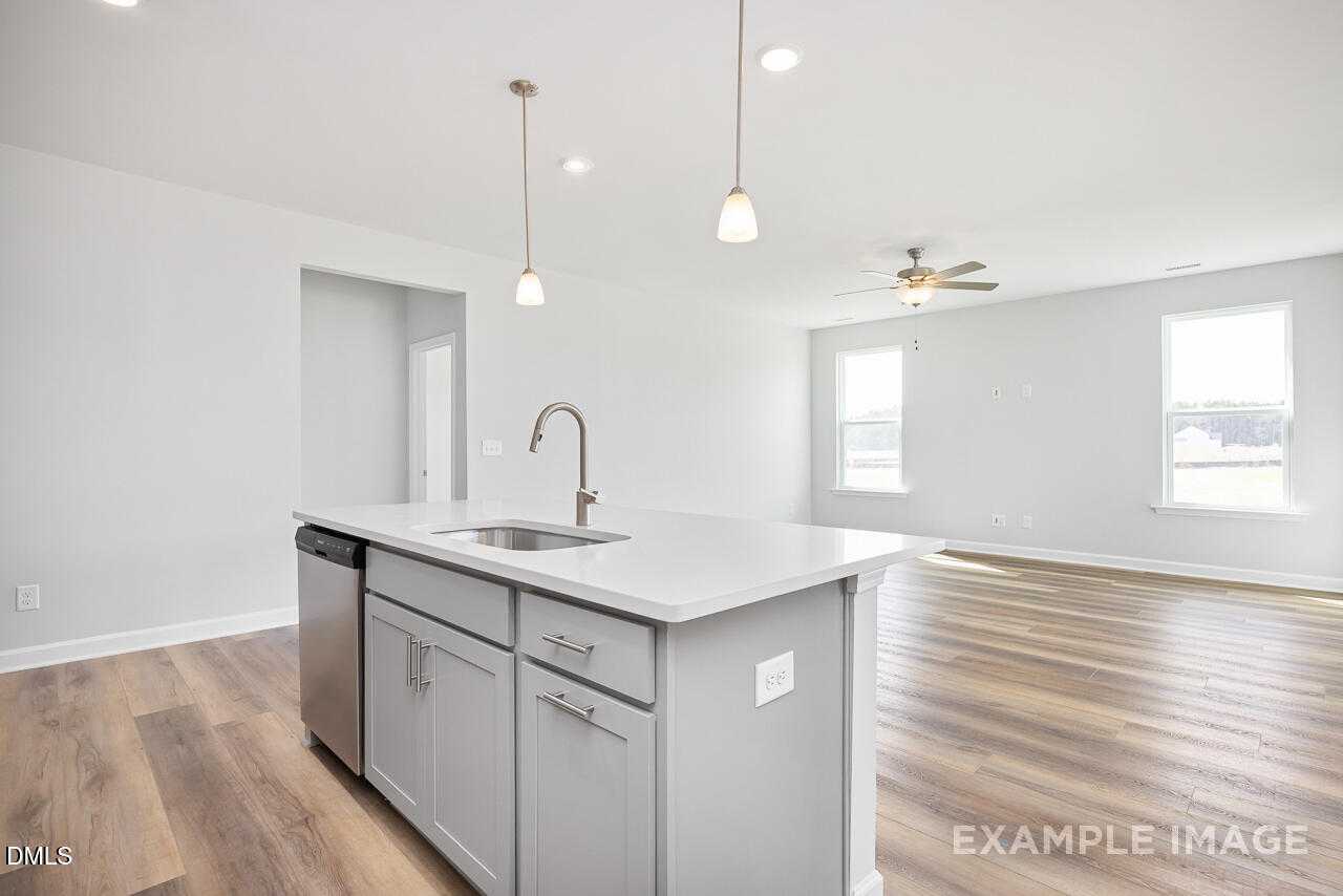 Open-concept kitchen with white quartz island, stainless sink, gray cabinets, hardwood floors in The Daphne C, Zebulon, NC