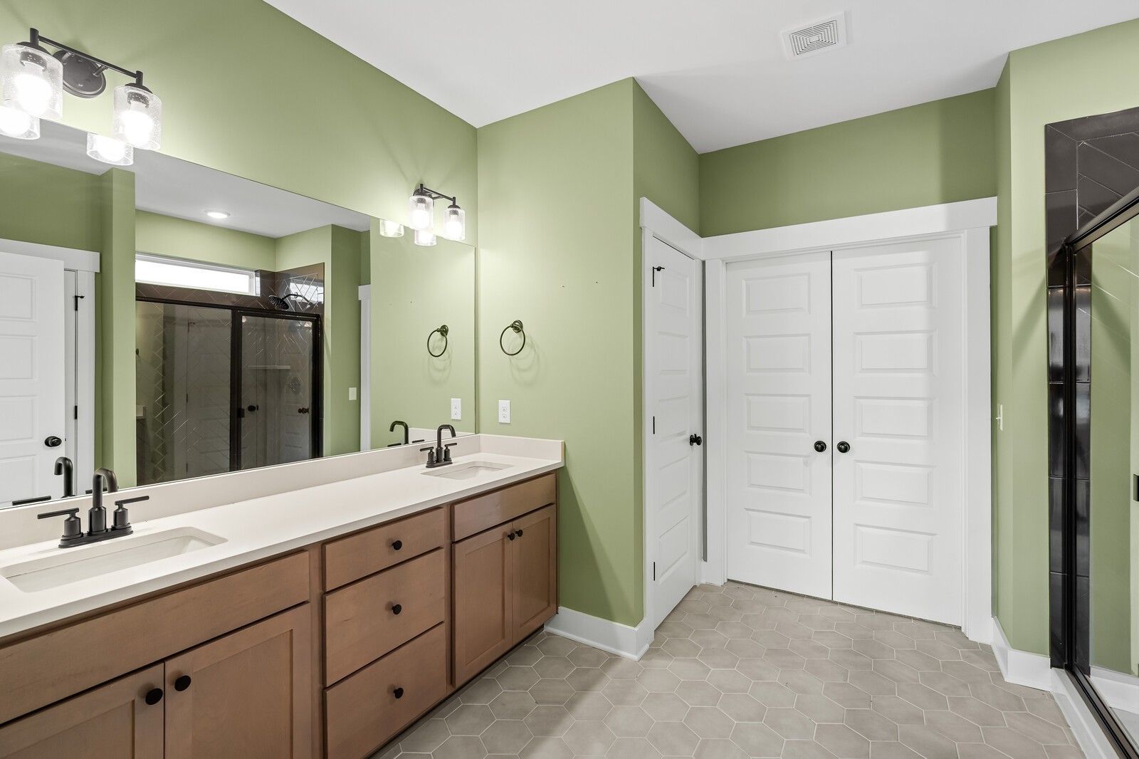 Modern master bathroom with sage green walls, double wood vanity, and glass shower in Davidson Homes The Ridgeport, Gallatin, TN