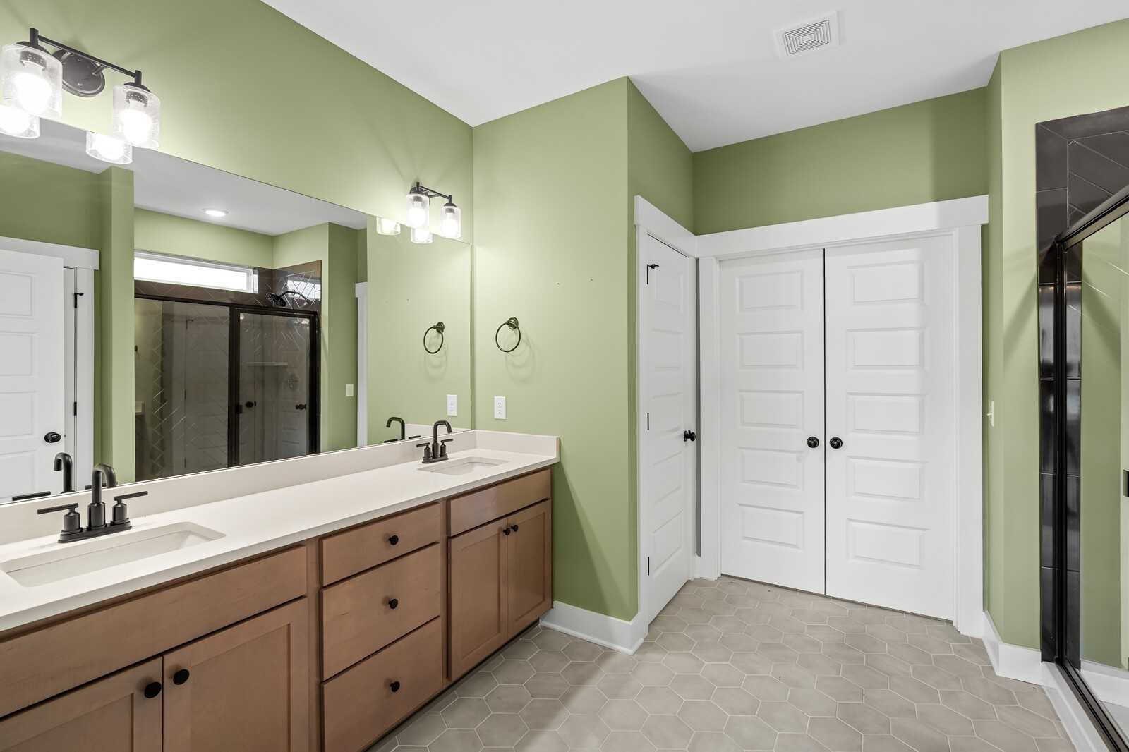 Modern master bathroom with sage green walls, double wood vanity, and glass shower in Davidson Homes The Ridgeport, Gallatin, TN