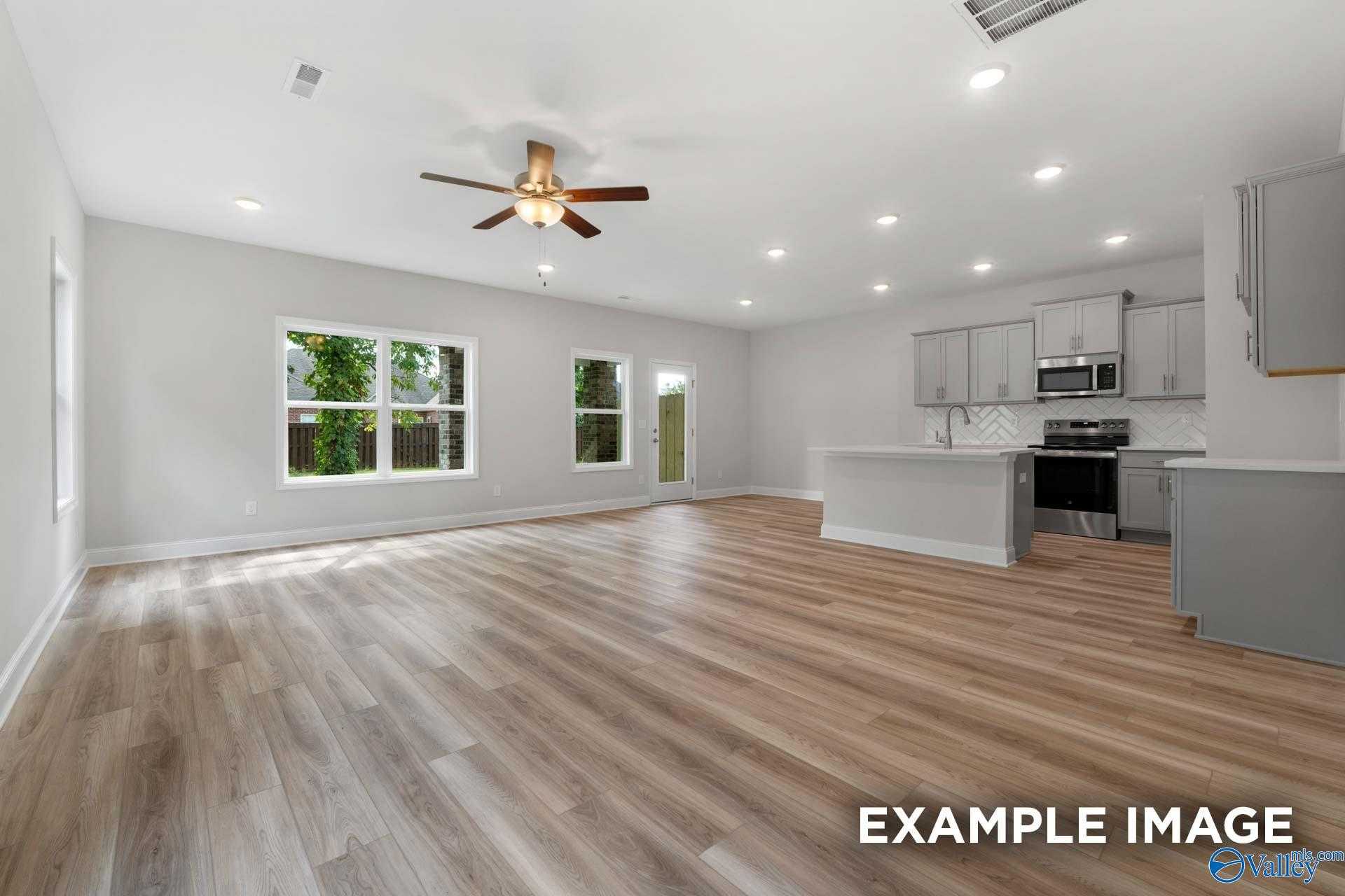 Open-concept kitchen and living area with gray cabinets, stainless steel appliances, hardwood floors, and large windows in The Camden, Huntsville home