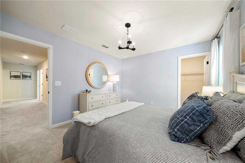 Cozy light blue bedroom with plush king bed, round mirror on white dresser, chandelier in 5-bedroom Davidson Homes The Hickory B, Riverwood, Dallas, Georgia