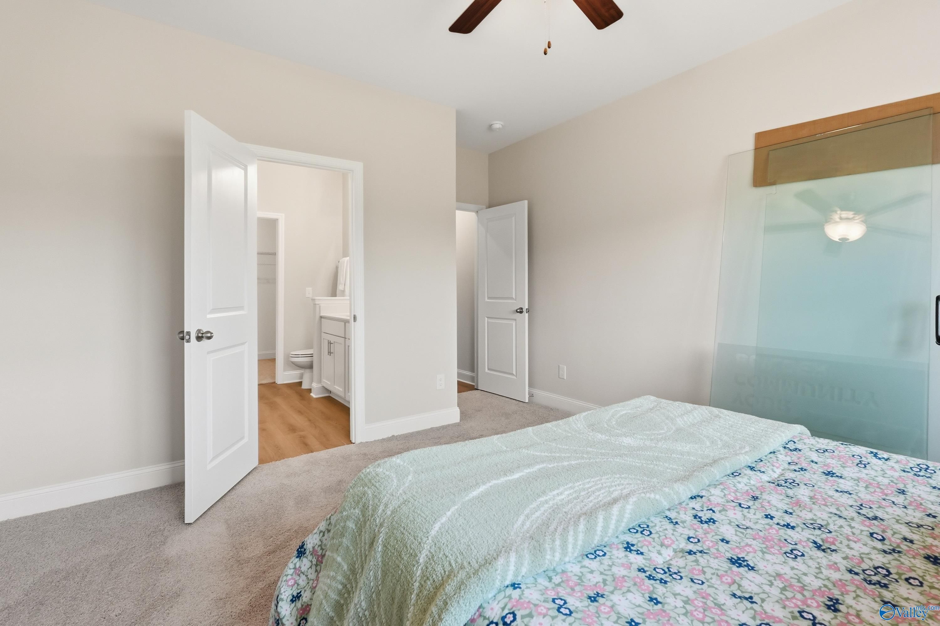 Cozy secondary bedroom with en-suite bath, ceiling fan, and floral quilted bed in Davidson Homes The Asheville, Toney, Alabama