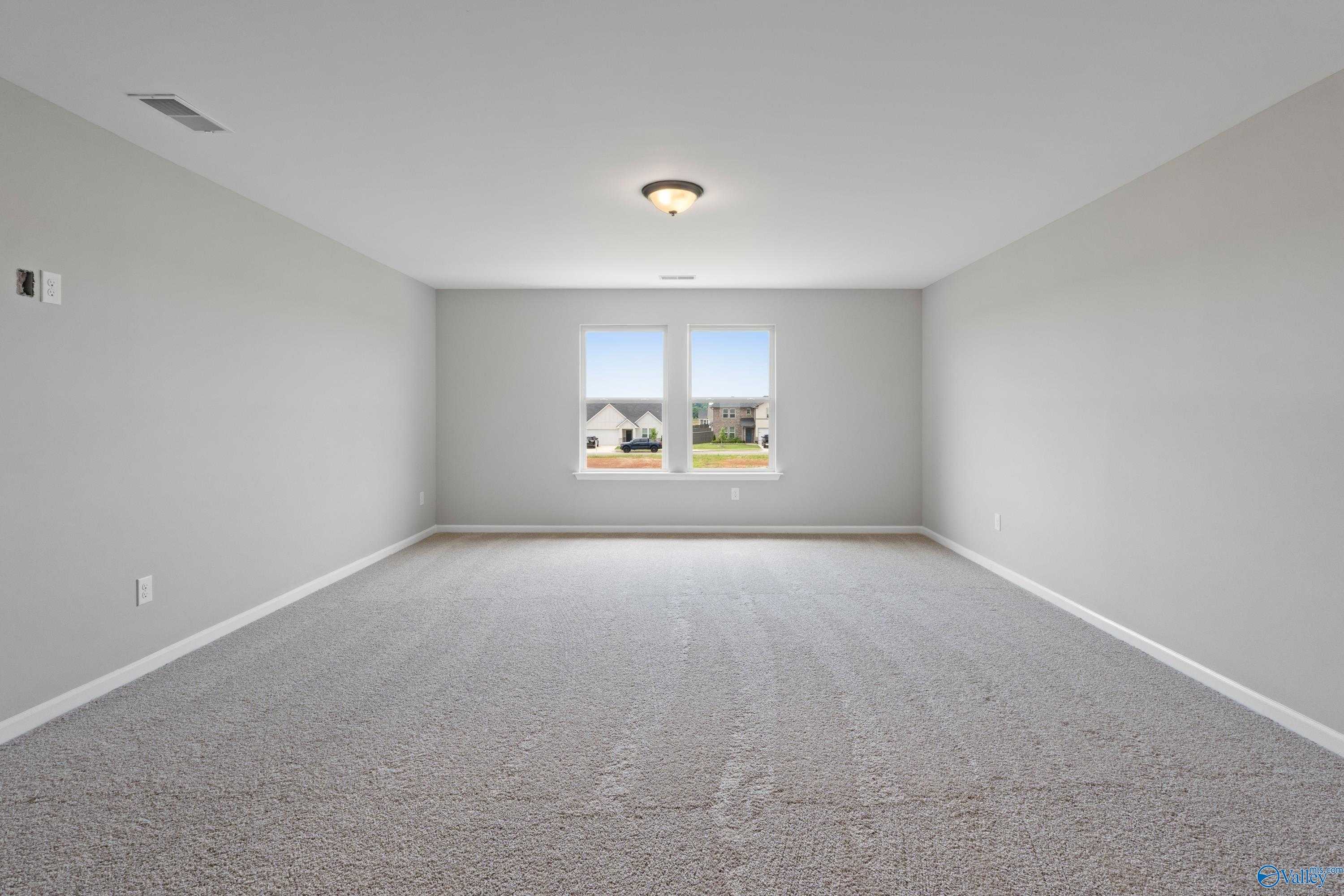 Empty bedroom with light gray walls, neutral carpet, and dual windows overlooking neighborhood in Davidson Homes The Dorado, Athens AL