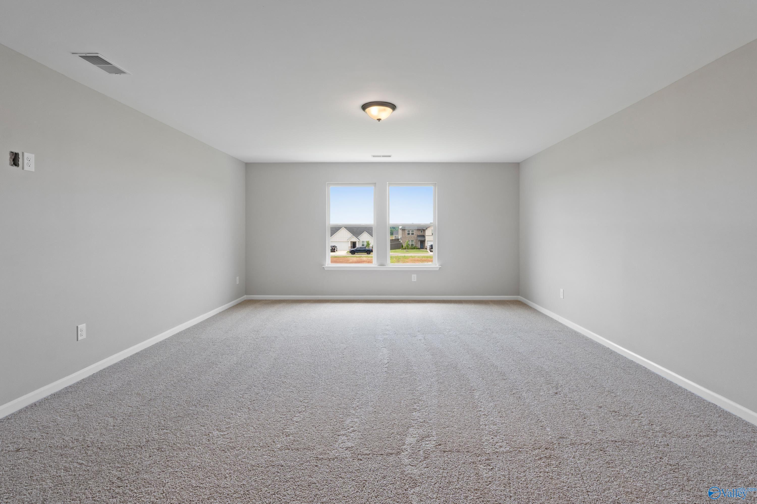 Spacious empty bedroom with gray walls, large double windows overlooking neighborhood, carpeted floor in Davidson Homes The Dorado, Athens AL