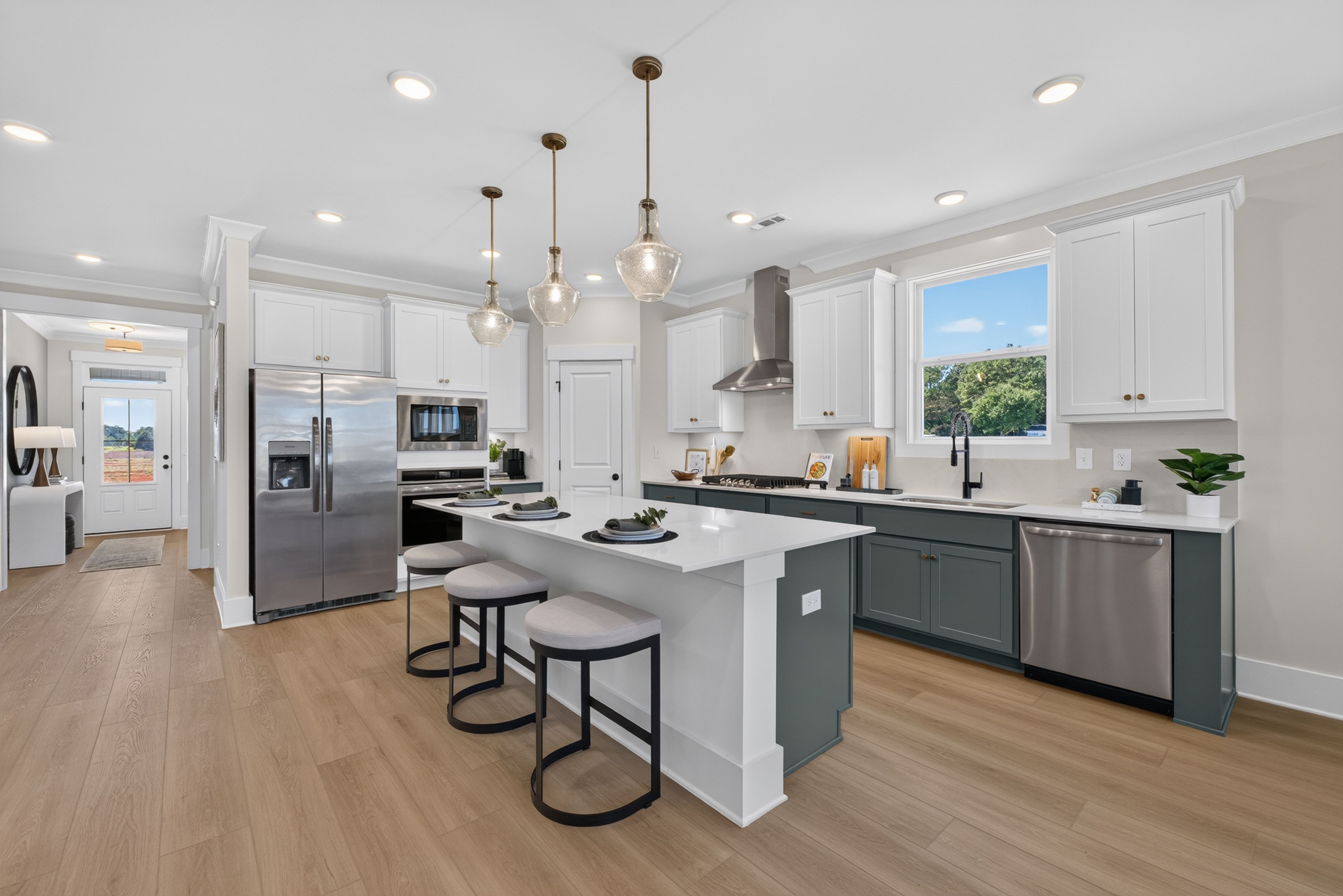Modern kitchen with white and green cabinets, island with bar stools, and stainless appliances at Evergreen Mill in Madison, AL