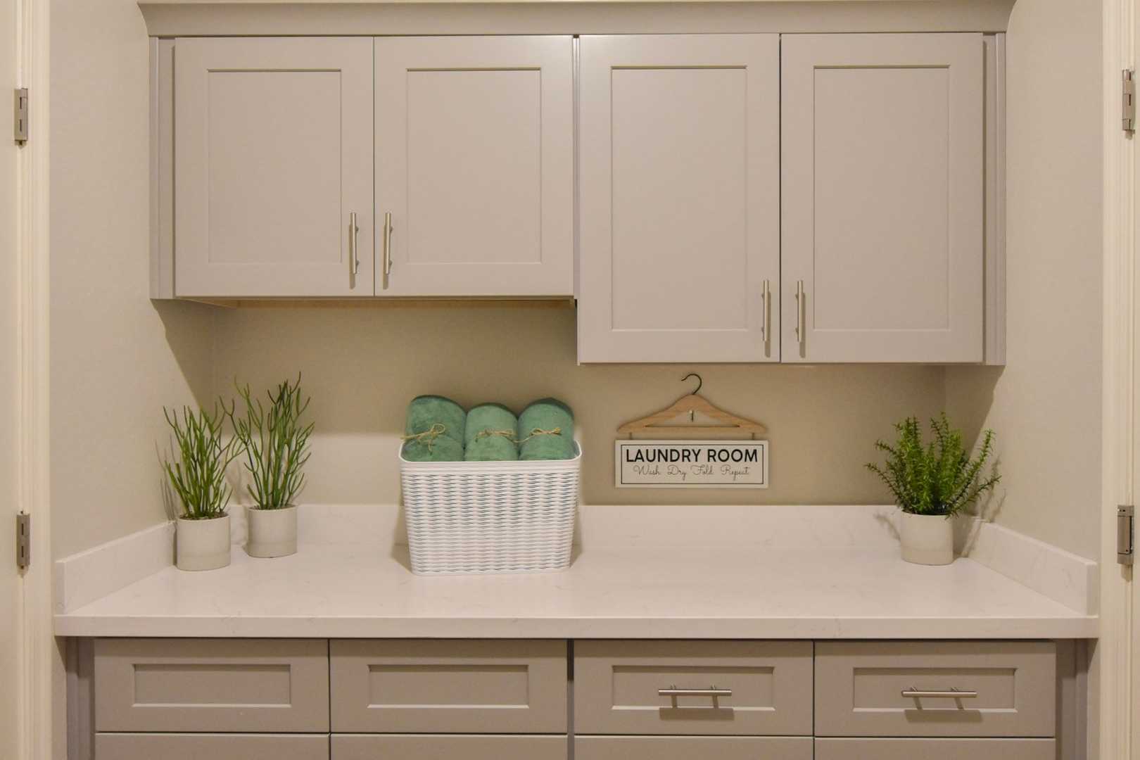 Spacious laundry room in The Harmony Davidson Homes design with beige shaker cabinets, white quartz countertop, green towels, and potted plants